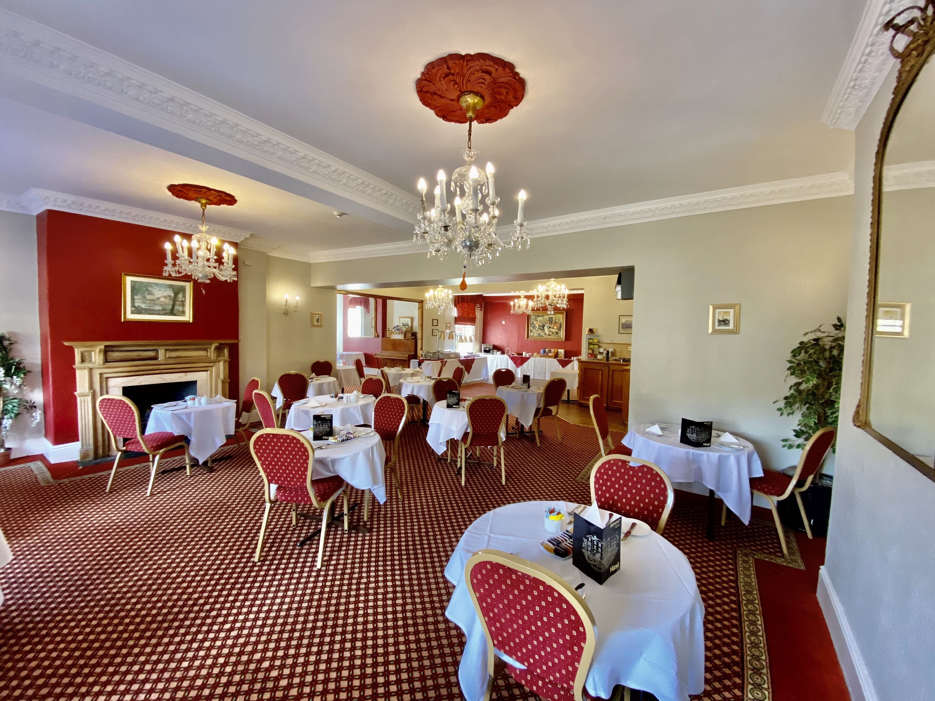 A dining area with round tables, red chairs, chandeliers, and a patterned carpet.