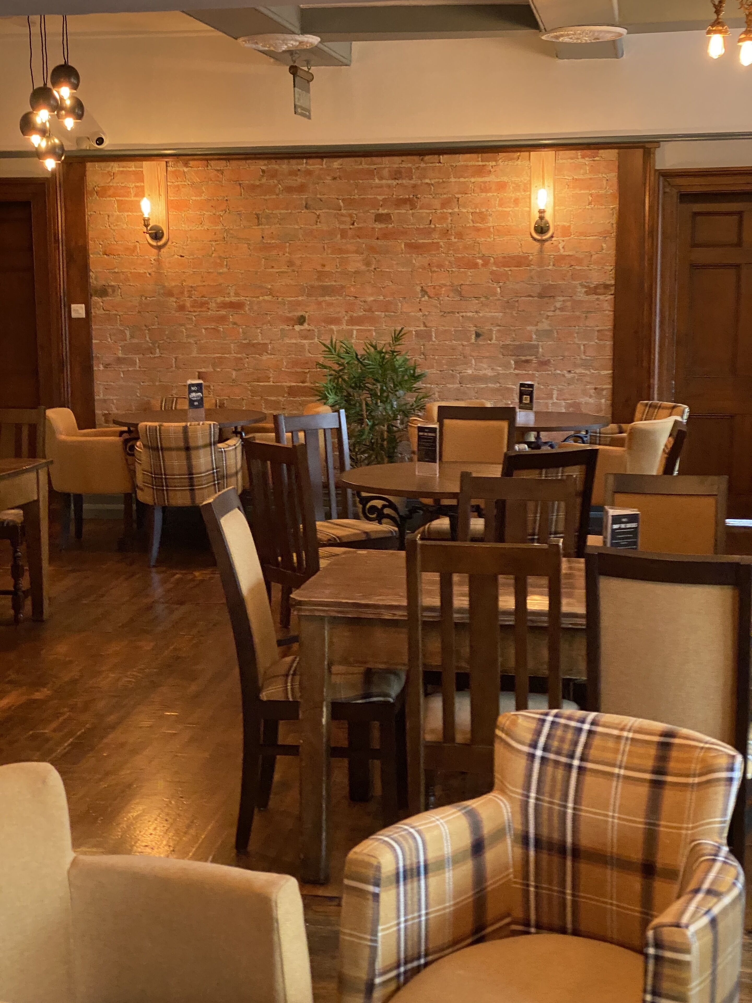 A cozy restaurant with brick walls, wooden tables, and plaid chairs.