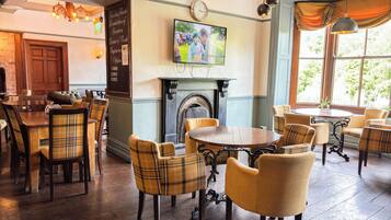 A dining area with wooden tables and chairs, a fireplace, and a television mounted on the wall.