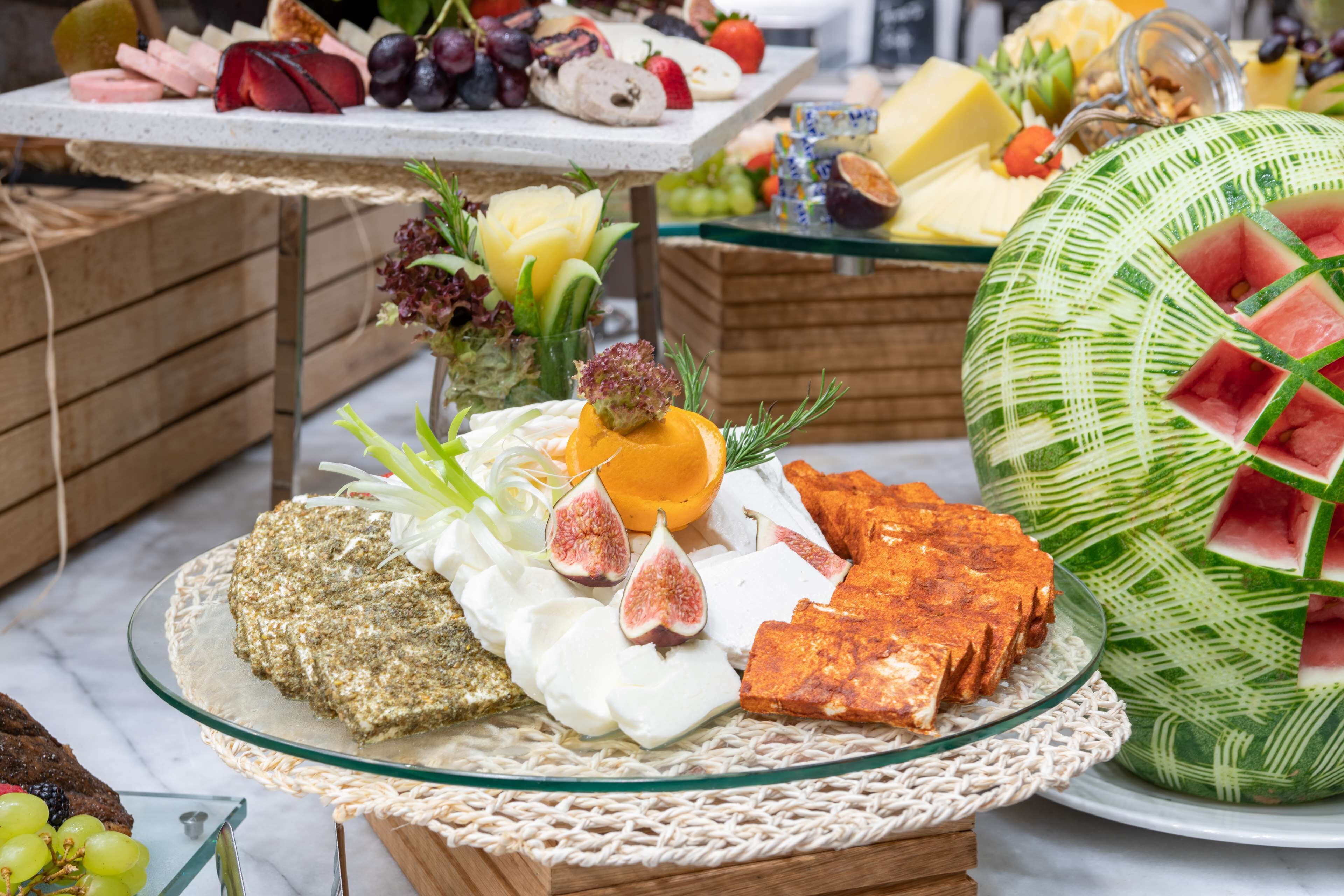 Un bufé con diferentes opciones de comida, incluyendo frutas, quesos y una sandía decorada.