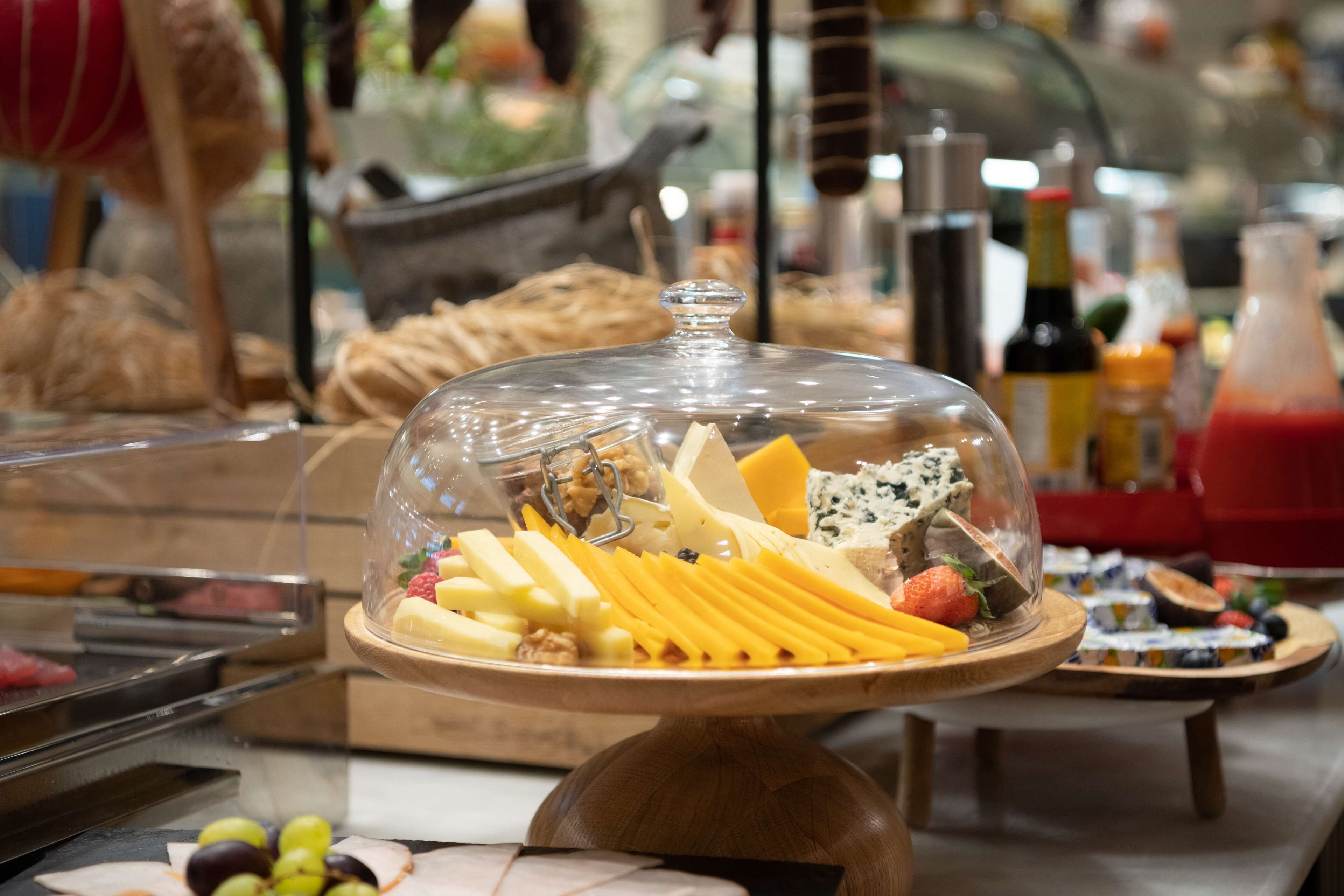 A buffet with various cheeses, fruits, and nuts under a glass dome.