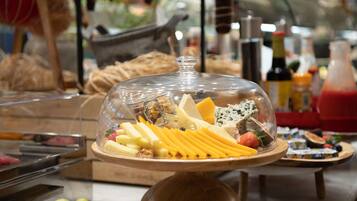 A buffet with various cheeses, fruits, and nuts under a glass dome.