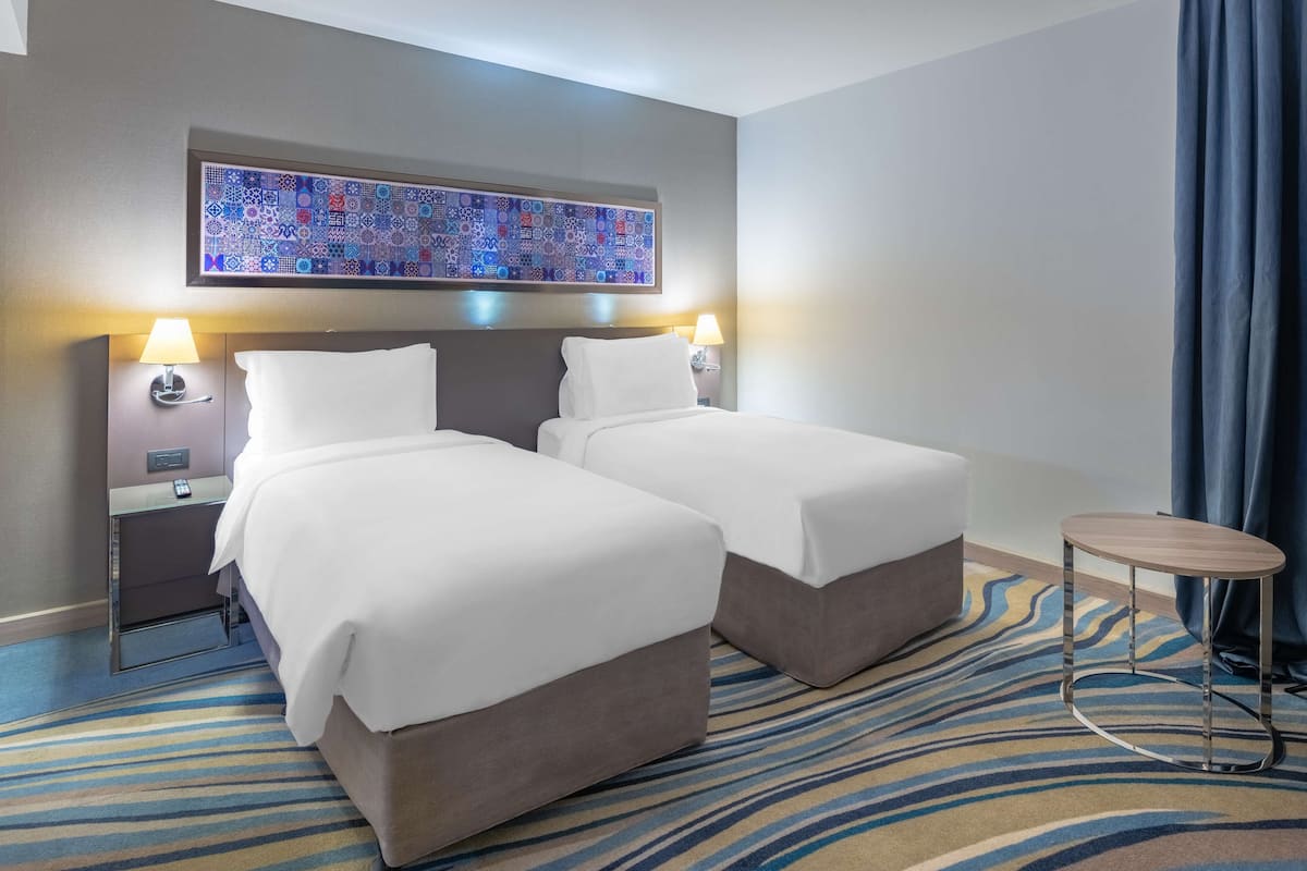 A hotel room with two beds, a patterned rug, a small round table, and a large abstract painting on the wall.