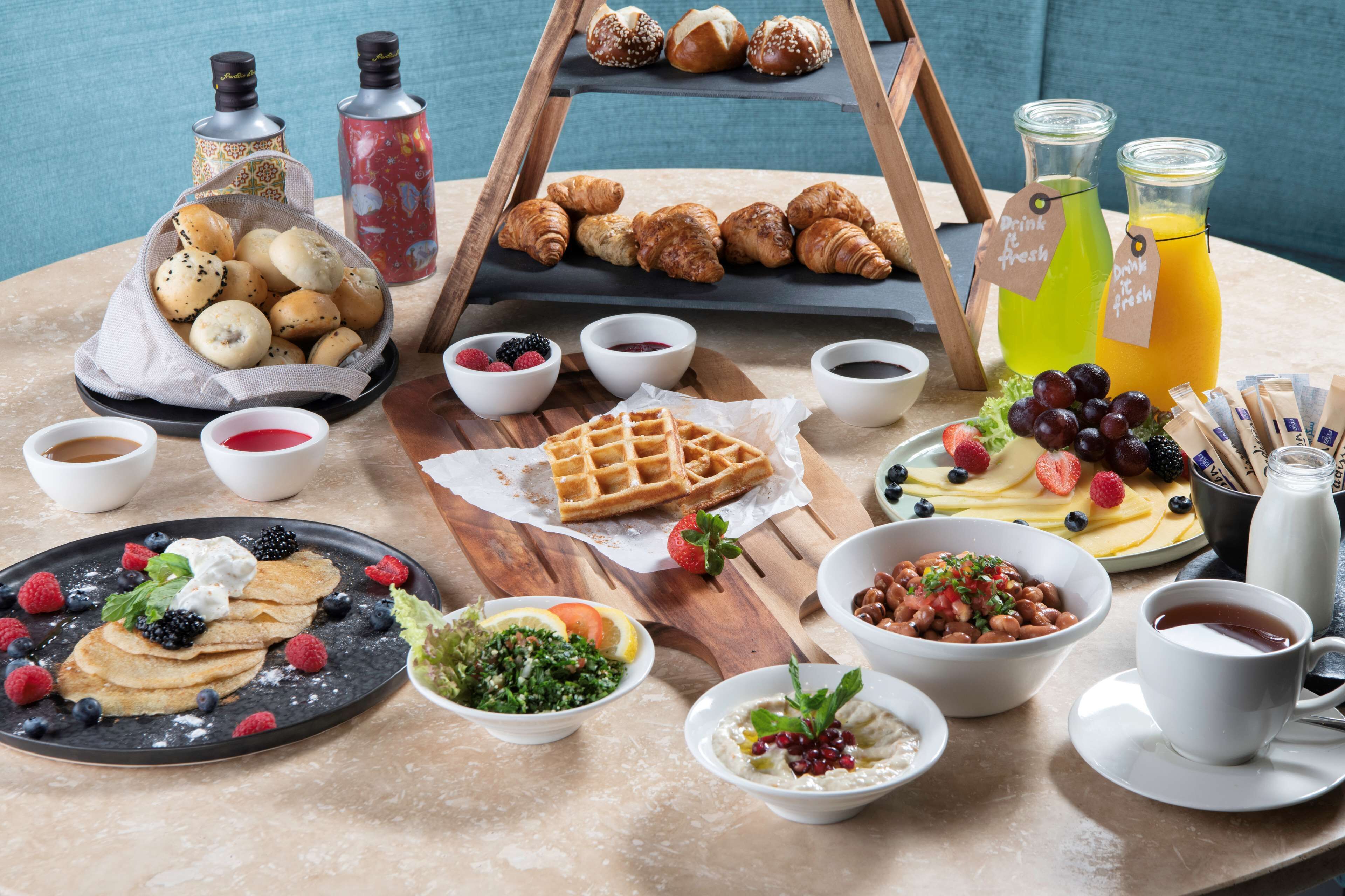 A breakfast buffet with pastries, waffles, and various fruits and beverages.
