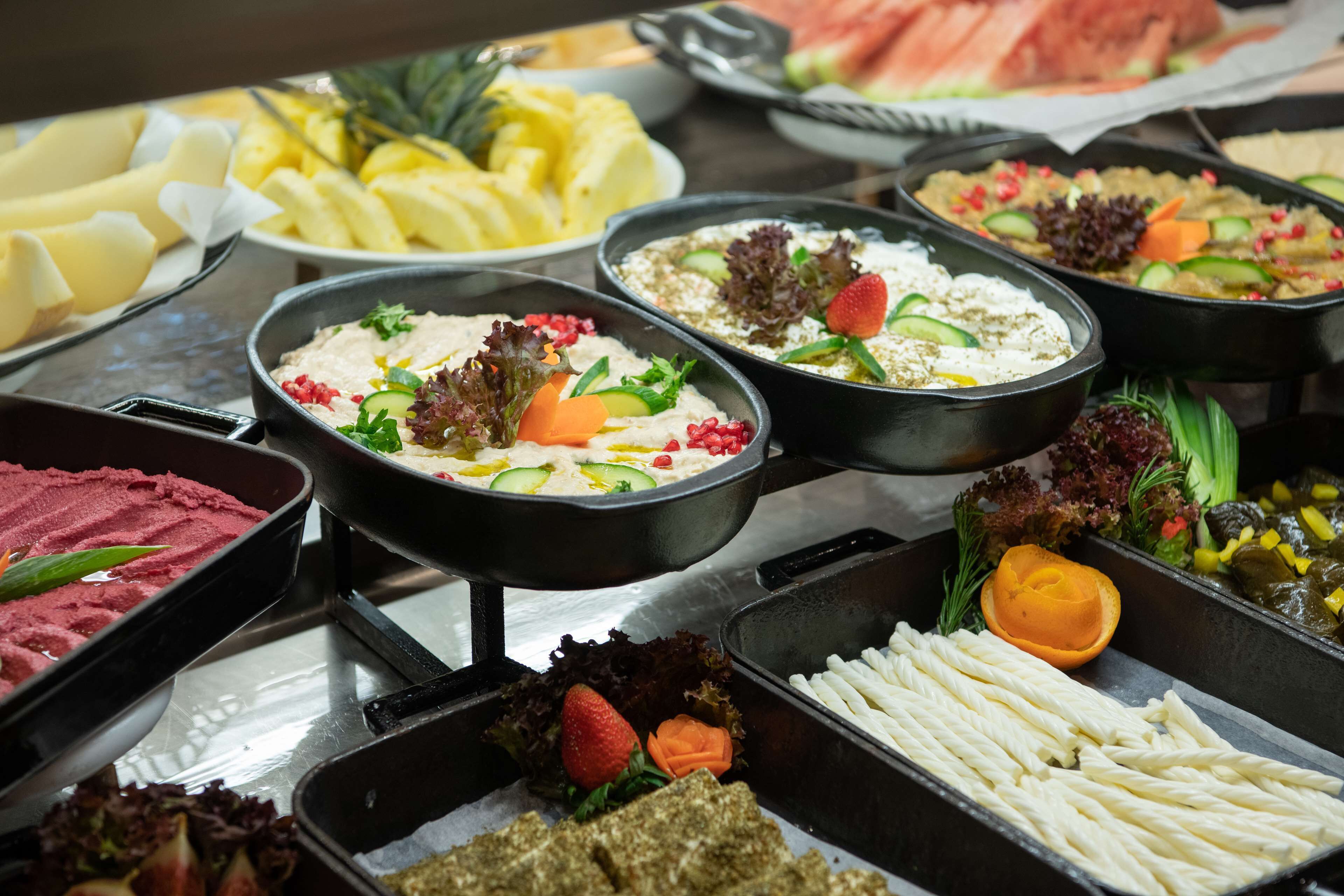 Un bufé con diversos platos, incluyendo salsas, frutas y verduras.