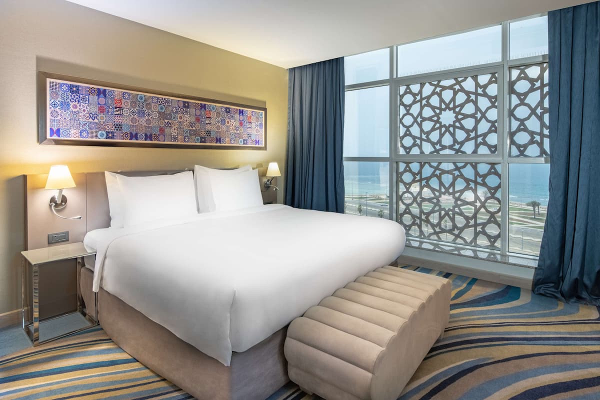 A hotel room with a large bed, a view of the beach, and a decorative wall piece.