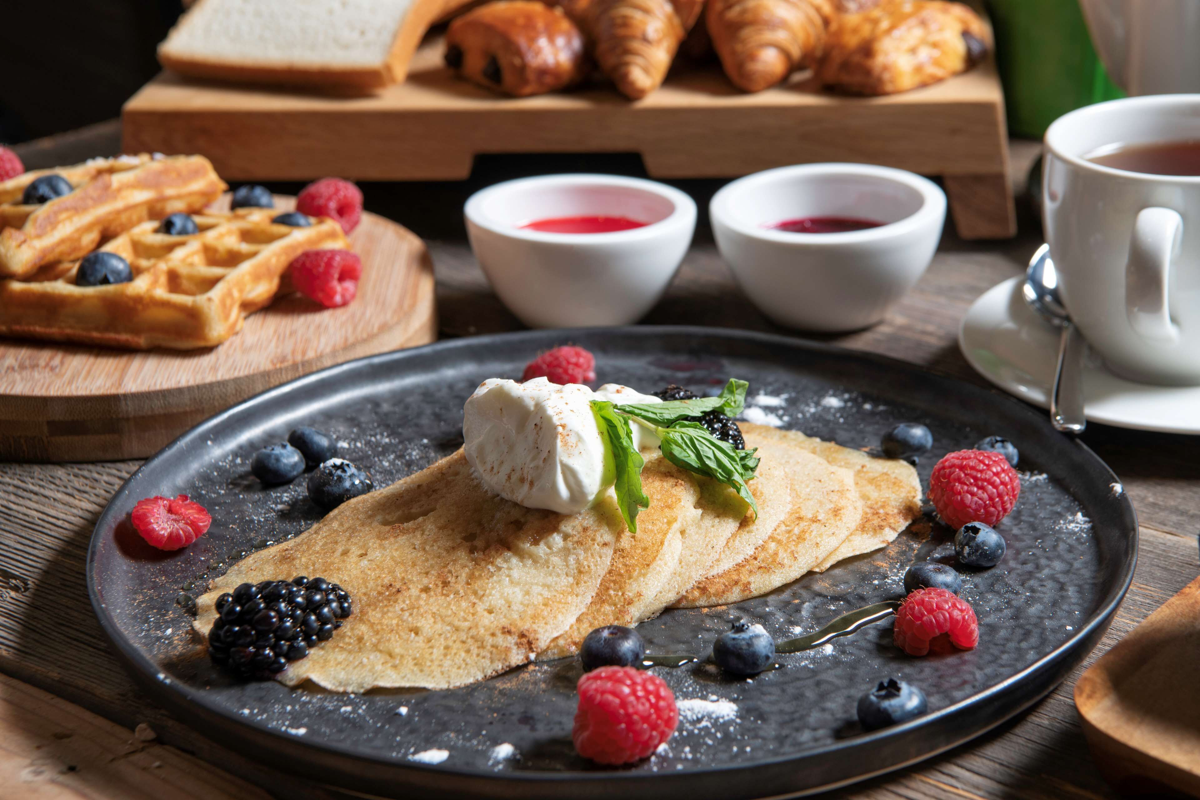 Un desayuno con gofres, crepes y bayas sobre una mesa de madera.