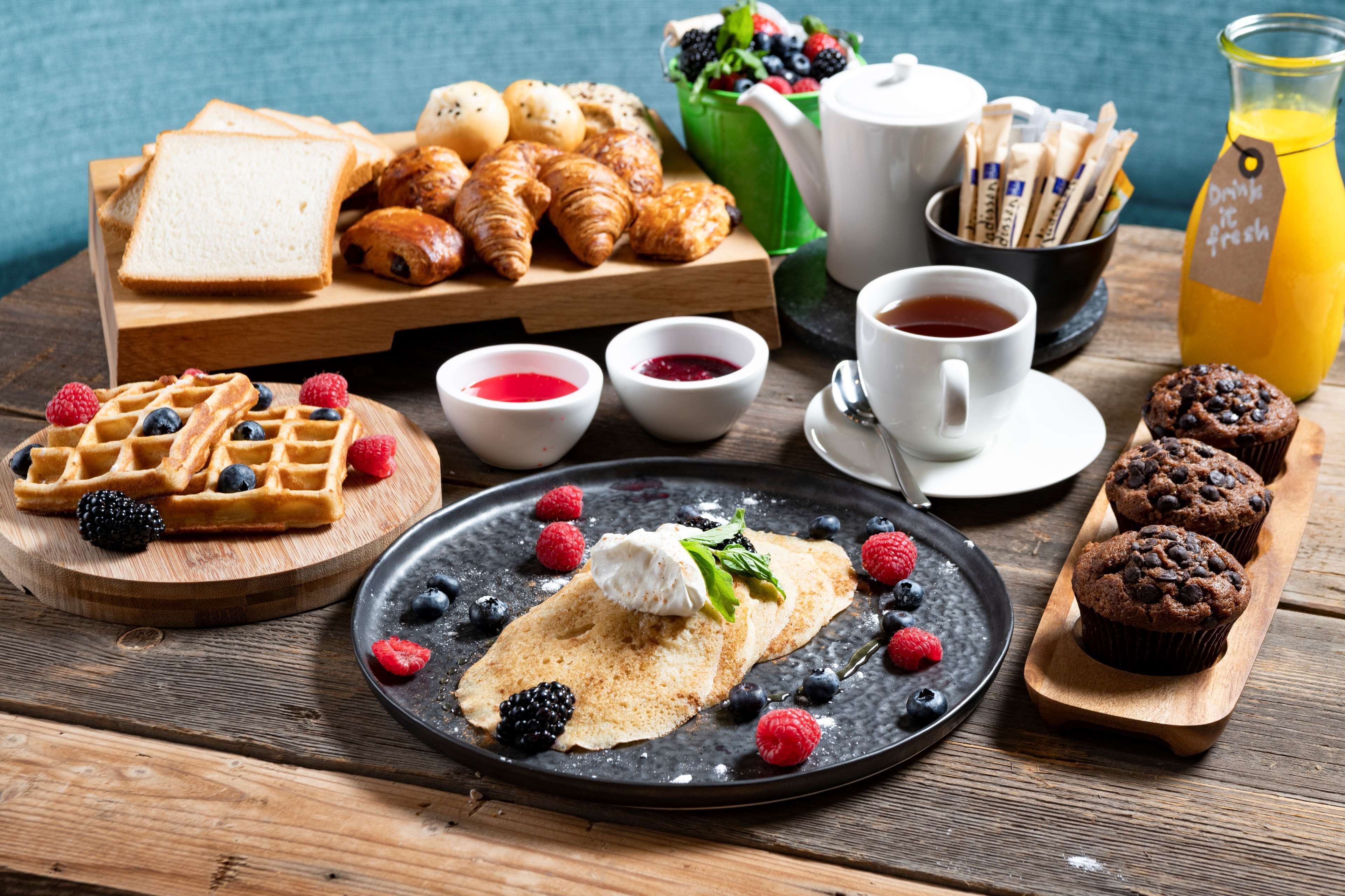 Un desayuno con waffles, cruasanes, muffins y frutos rojos frescos.
