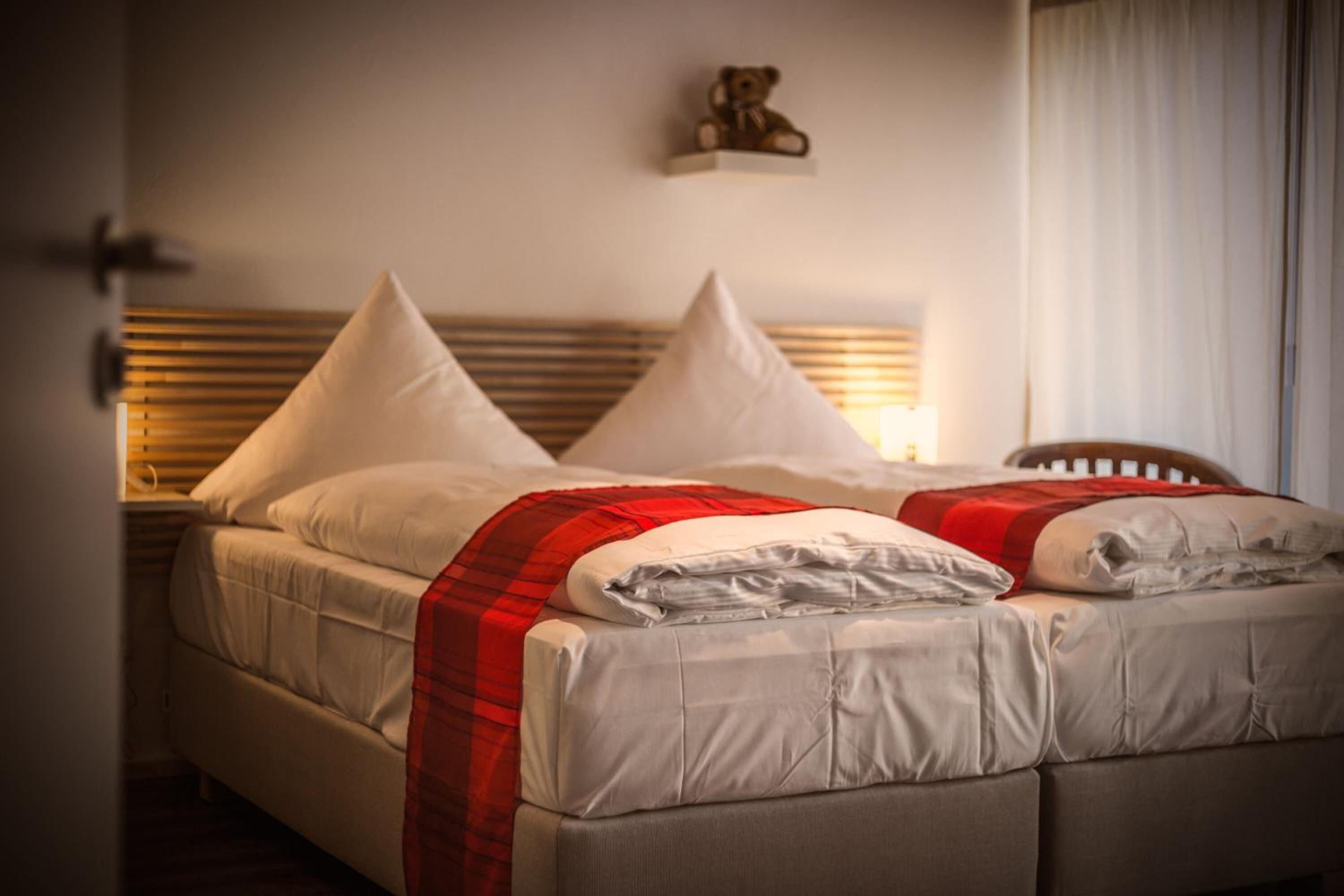 A double bed with a red and white blanket, two white pillows, and a wooden headboard.