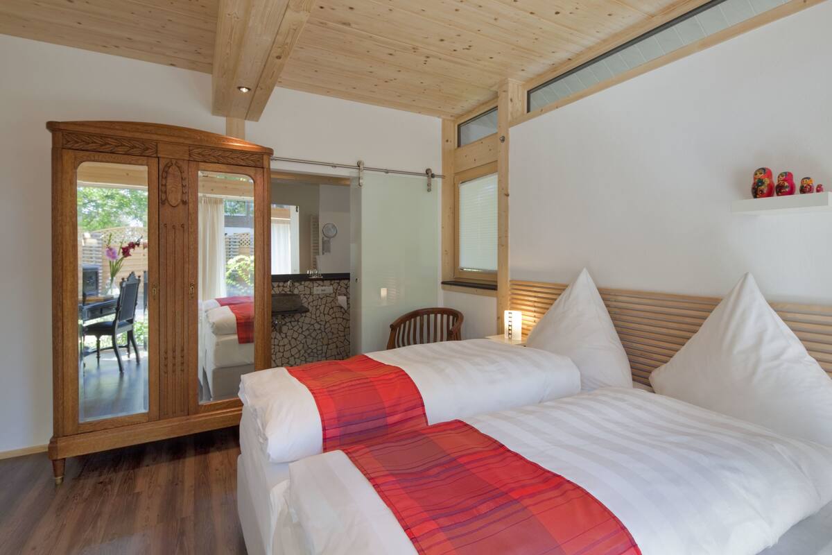 Quarto com duas camas, guarda-roupa de madeira, espelho e uma pequena estante com objetos decorativos.