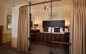 A four-poster bed with a plaid bedspread, a nightstand with a lamp, and a painting on the wall.
