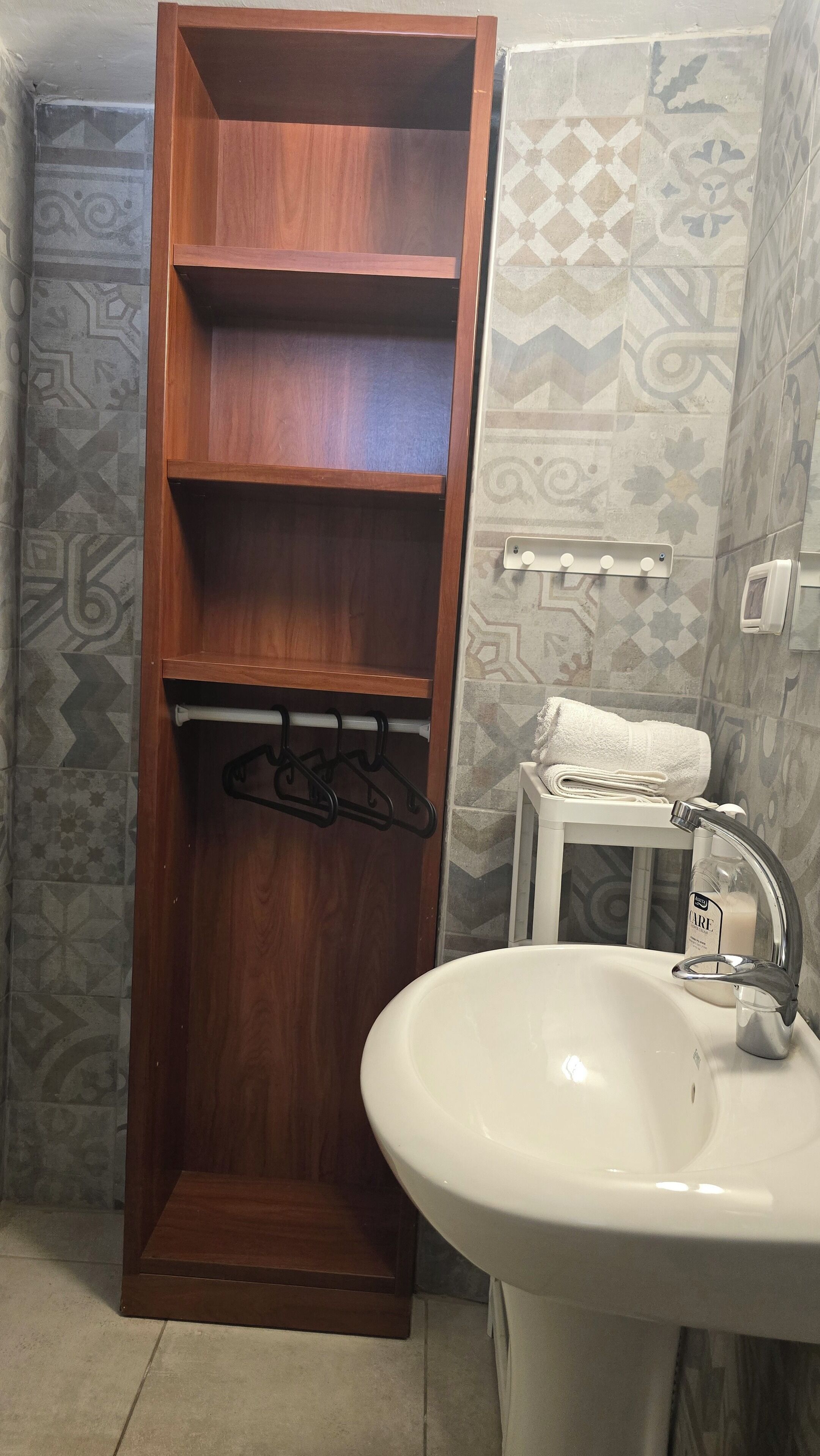 A bathroom with a wooden shelf unit, a white sink, and patterned tiles.