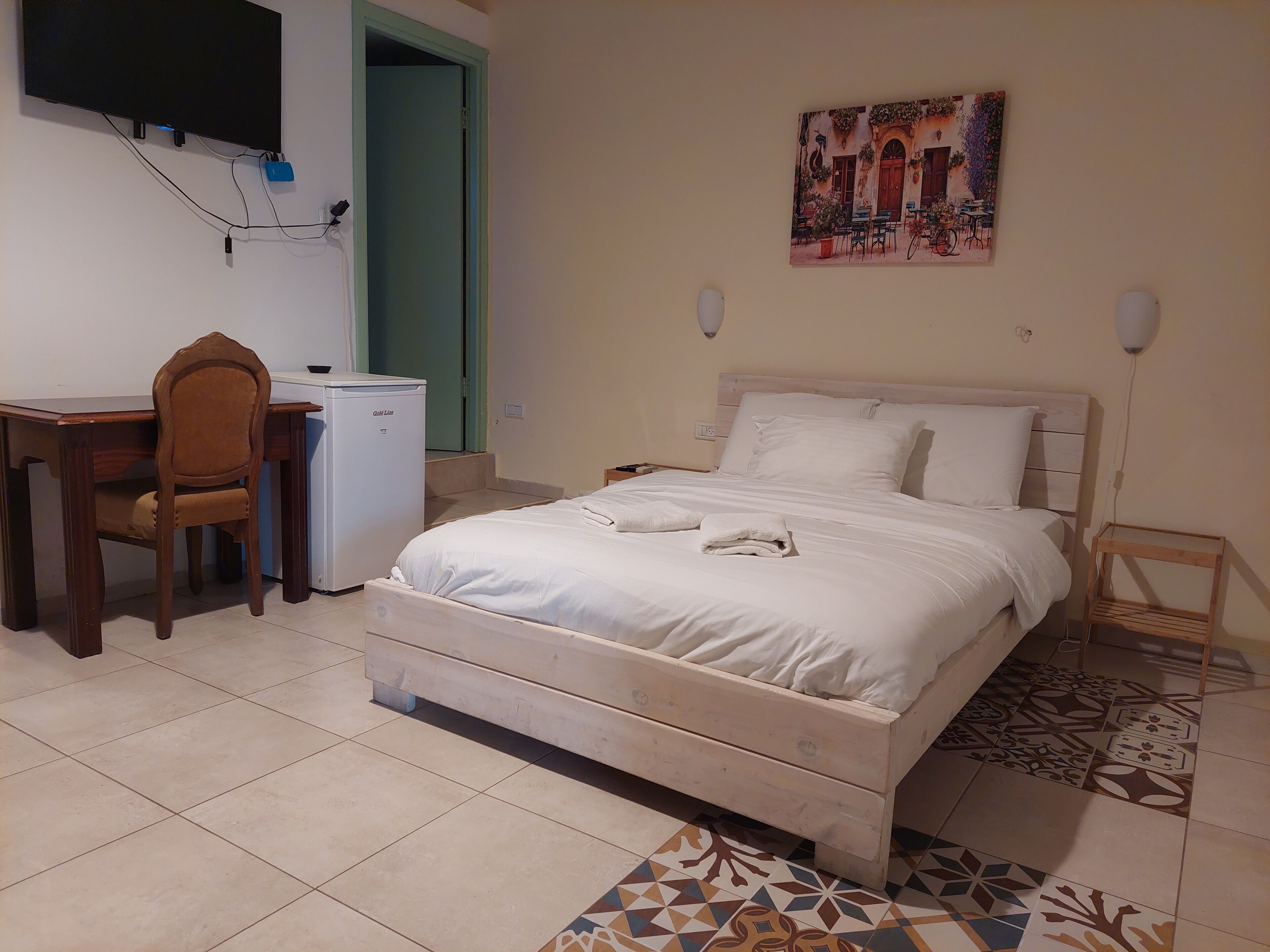 Une chambre à coucher avec un lit, un bureau, une chaise, un petit réfrigérateur et un tableau accroché au mur.