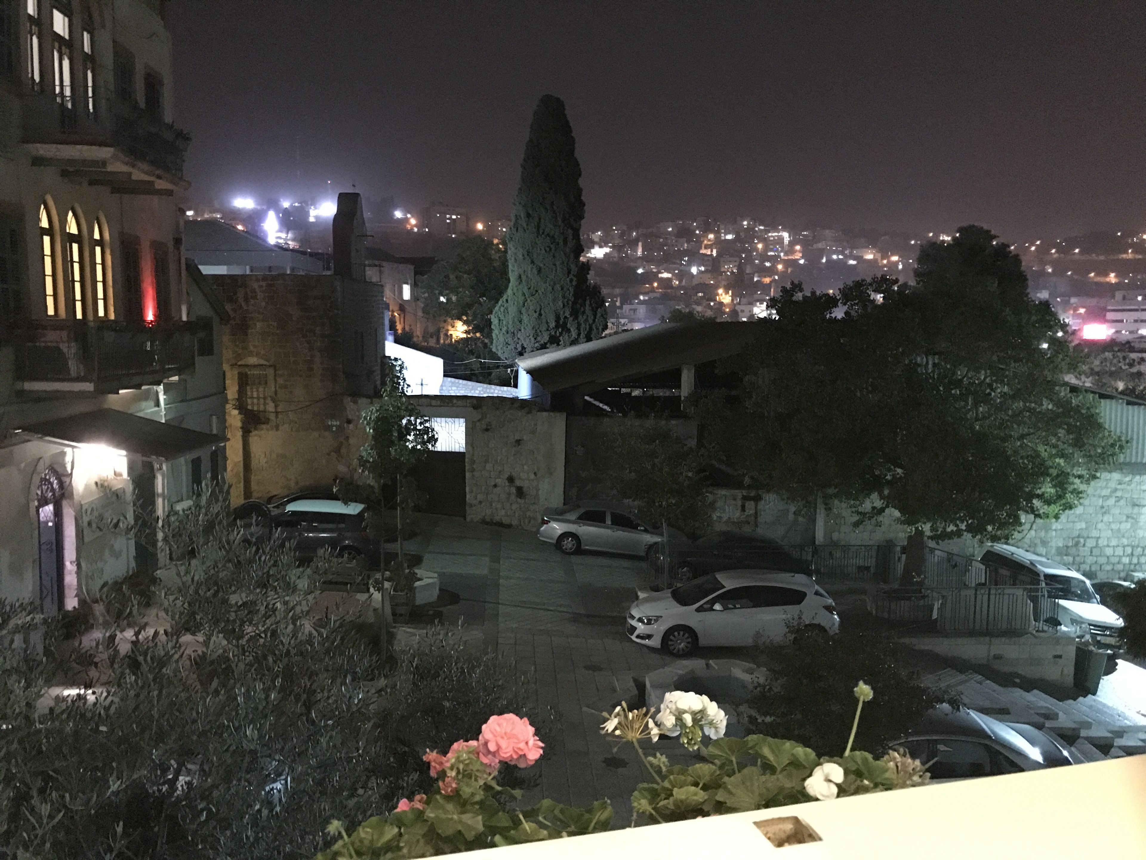 Vue nocturne d’un quartier résidentiel avec des voitures garées, une église et un paysage urbain en arrière-plan.