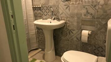 Un baño con lavamanos pedestal, inodoro, baldosas estampadas y un tapete verde a rayas.