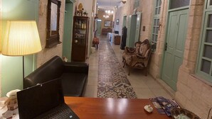 A narrow hallway with a patterned floor, a wooden table with a laptop, a lamp, and a bowl on the table. - Al Bishara Guest house (Nazareth)