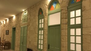 A hallway with stone walls, green doors, and a patterned carpet. - Al Bishara Guest house (Nazareth)
