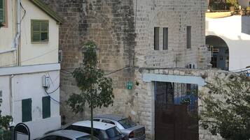 A street view with parked cars, a stone building with a gate, and a pink structure with a cross on top.