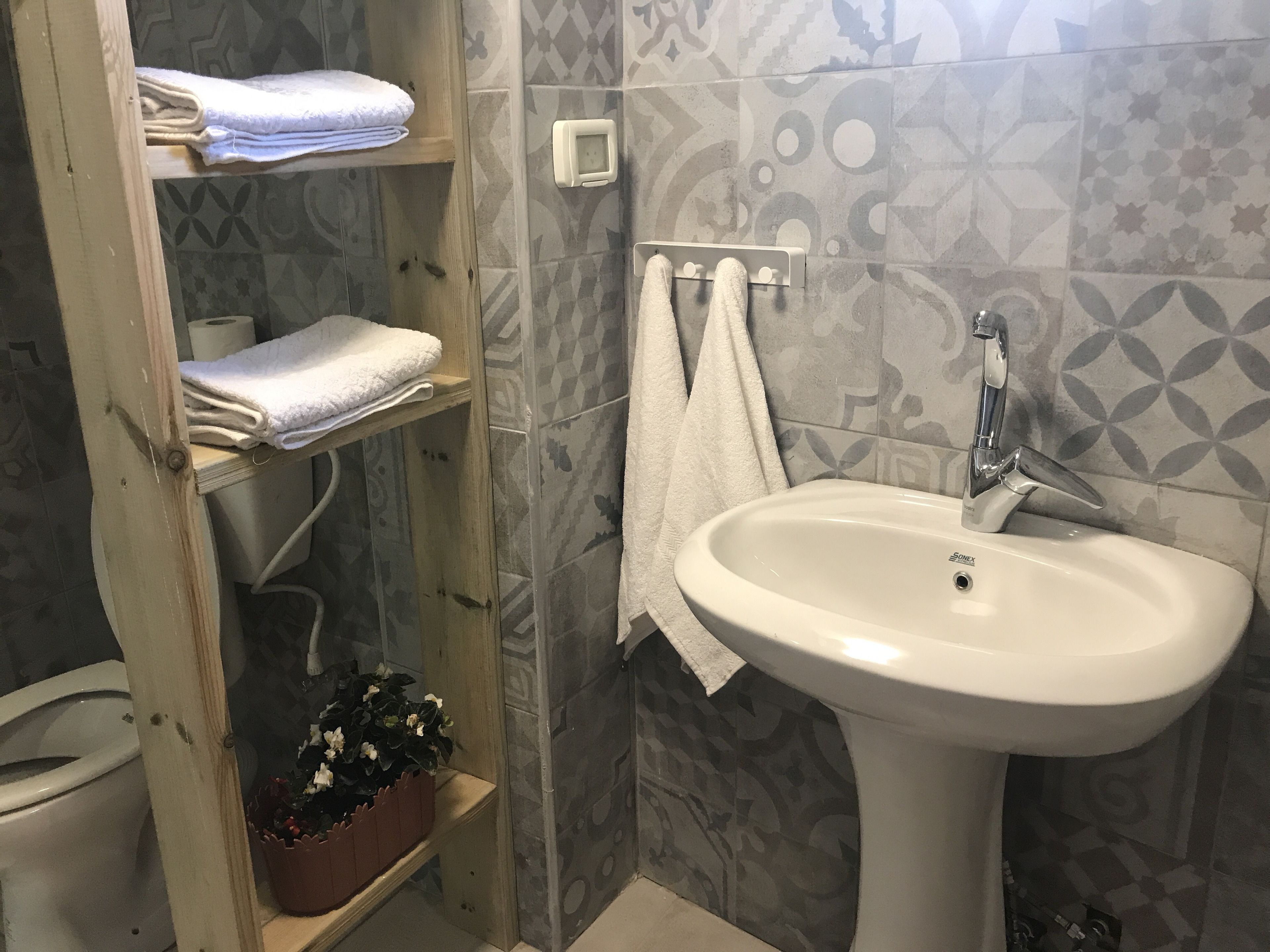 Un baño con un lavamanos blanco, un perchero para toallas y un estante con toallas dobladas.