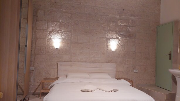 A bedroom with a wooden bed, white bedding, a green door, and a tiled floor. - Al Bishara Guest house (Nazareth)