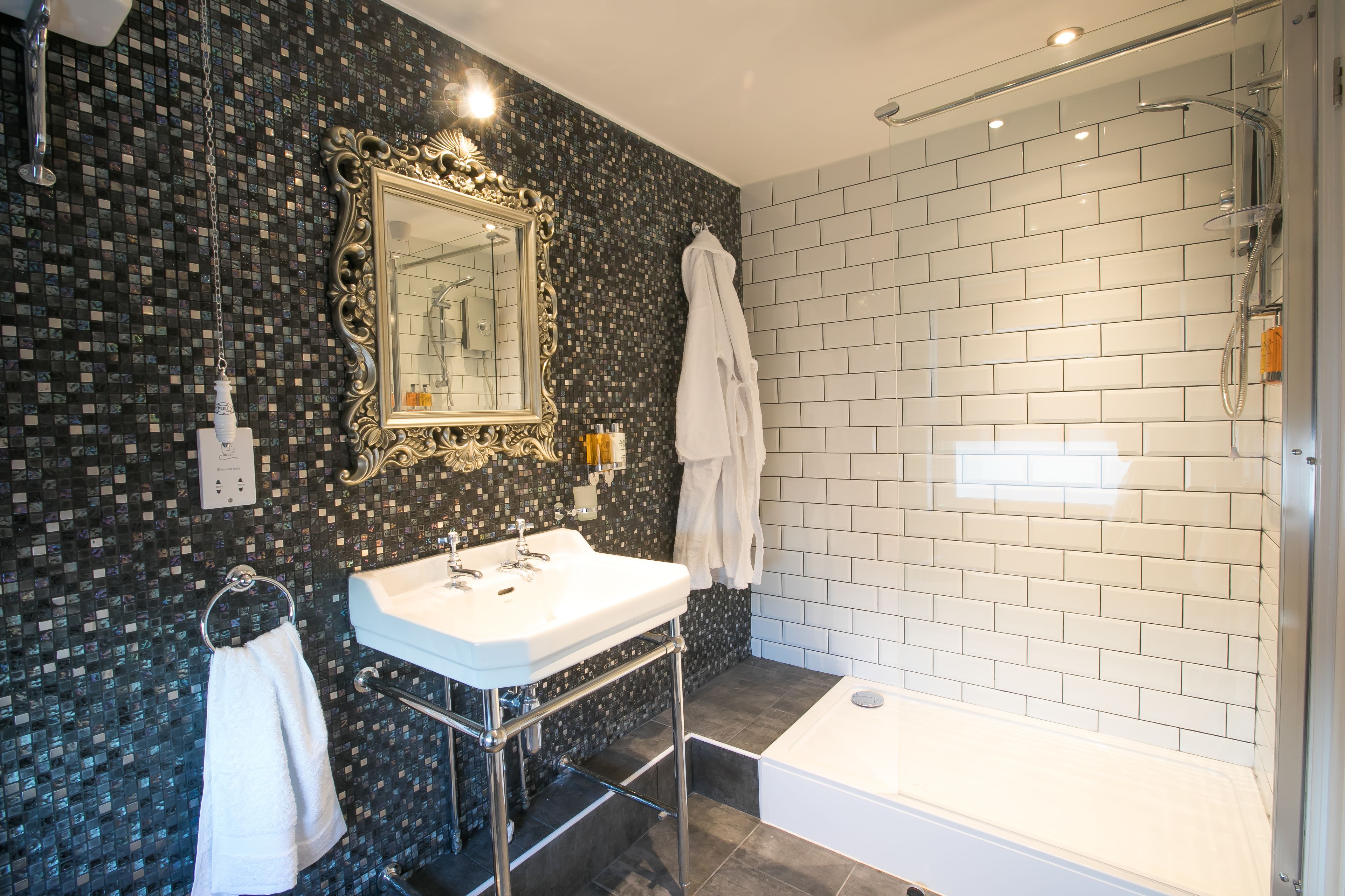A modern bathroom with a mosaic tile wall, a white sink, a large mirror, and a walk-in shower.