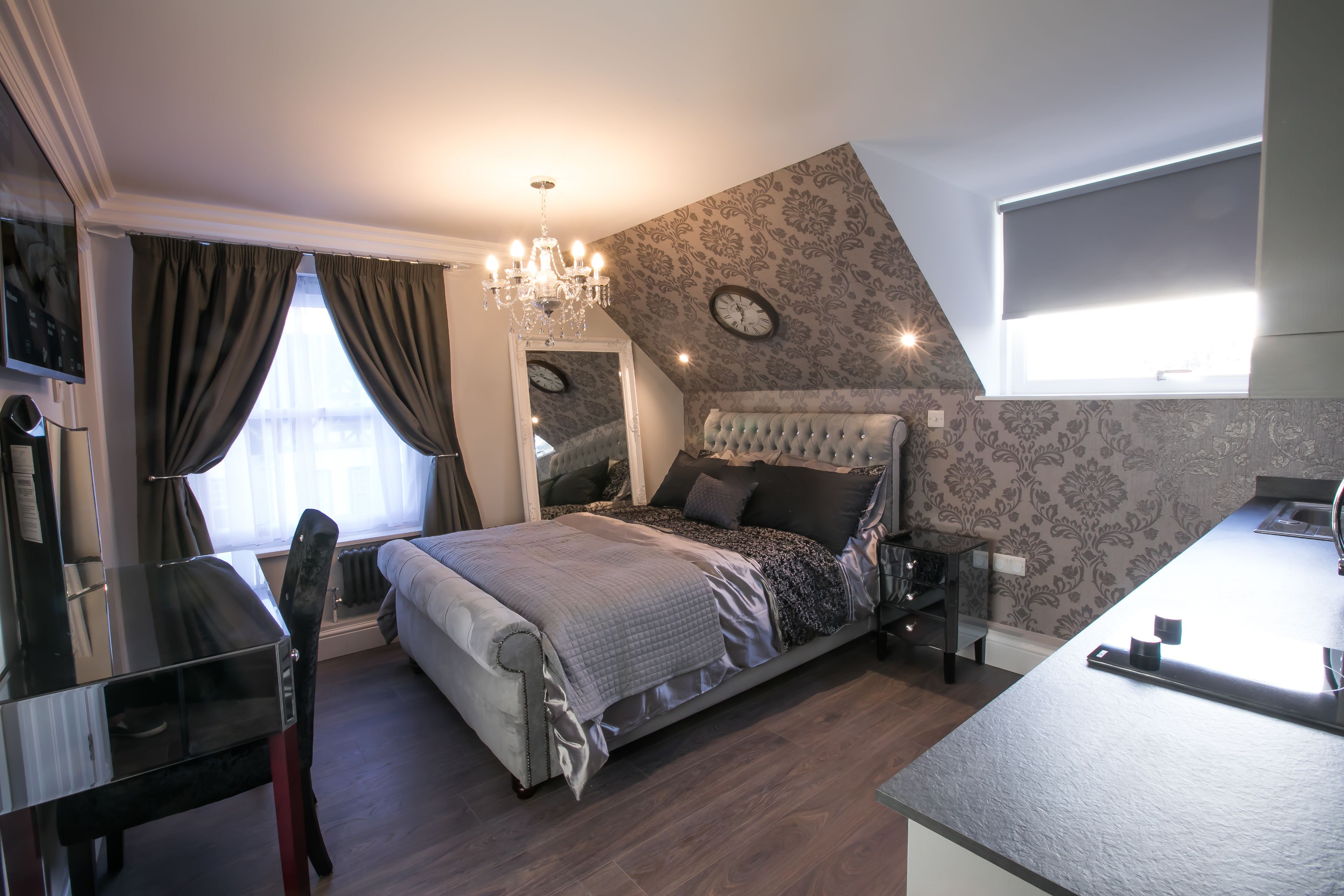 Une chambre à coucher avec un lit, un bureau, une chaise, un lustre, une horloge et une fenêtre.