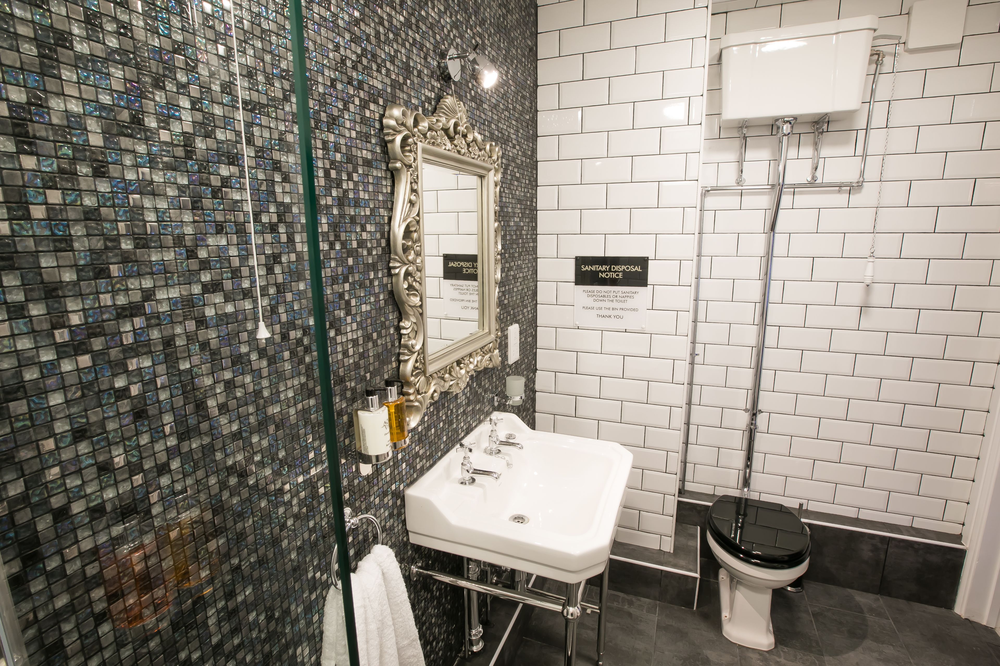 A bathroom with a glass shower enclosure, a white sink, and a black toilet.