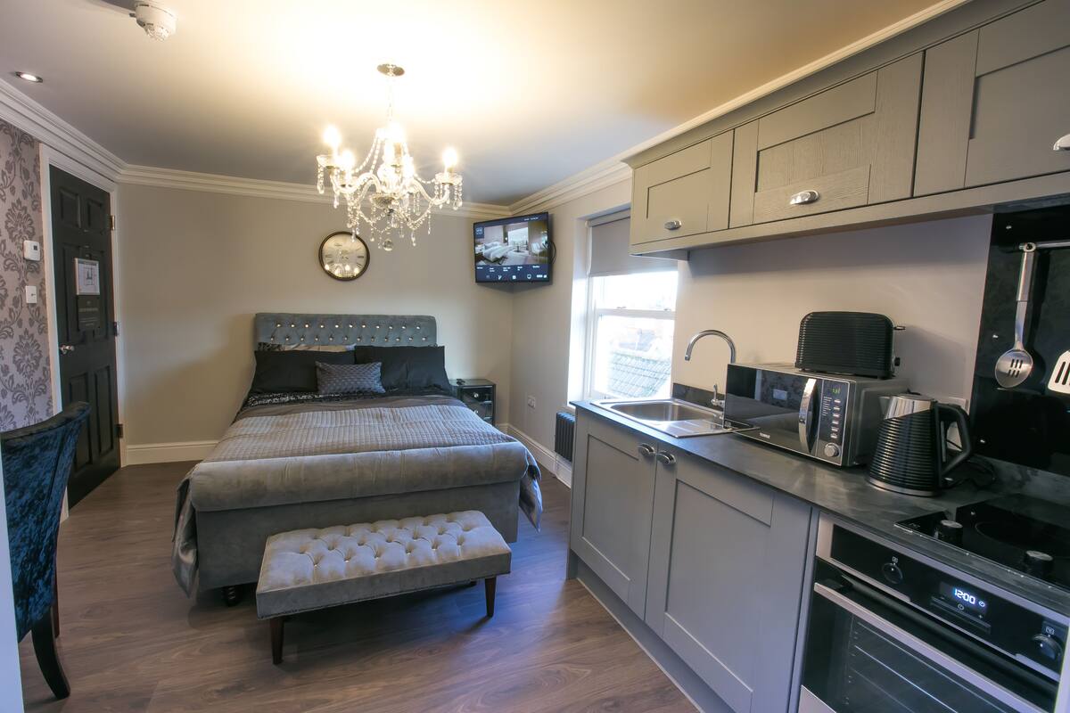 A modern bedroom with a large bed, a bedside table, a bench, and a TV mounted on the wall.