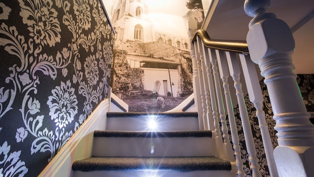 A staircase with a black and white patterned wall, a white balustrade, and a view of a building with a bell tower. - Number 10 The Abbey (Wymondham)
