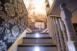 Una escalera con un muro estampado en blanco y negro, una barandilla blanca y vistas de un edificio con una torre de campanas.
