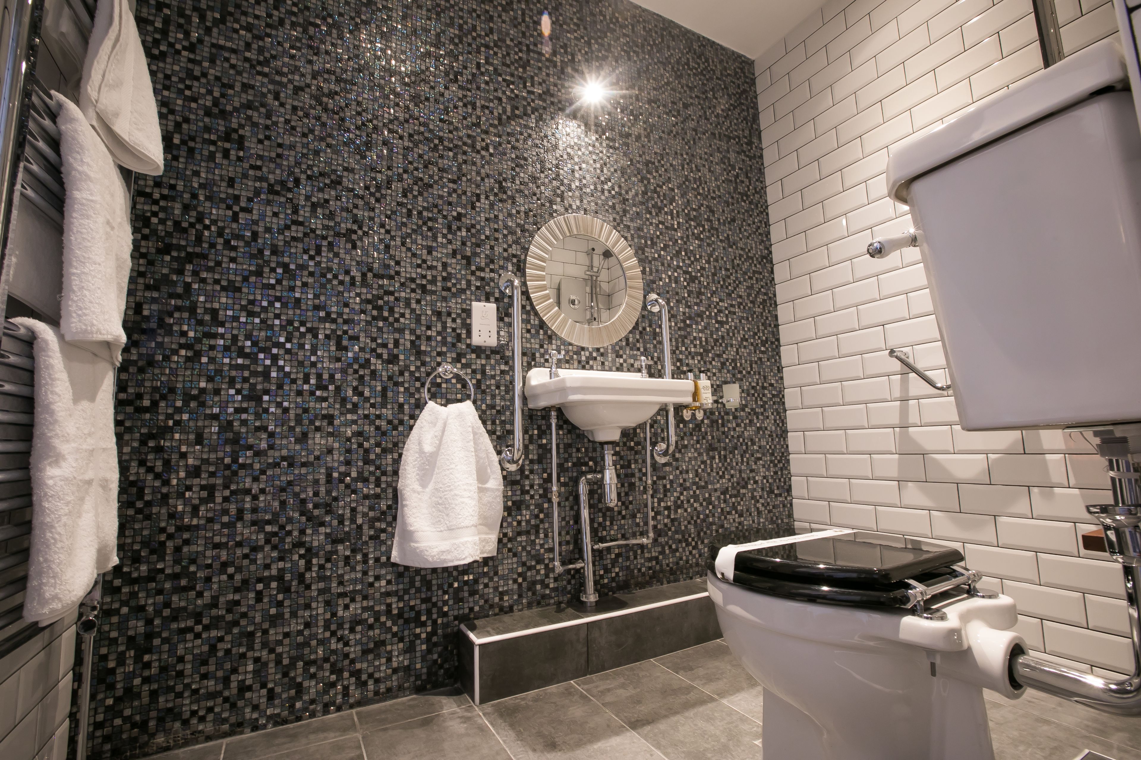 Ein modernes Badezimmer mit einer Wand aus Mosaikfliesen, einem weißen Waschbecken und einer Toilette.