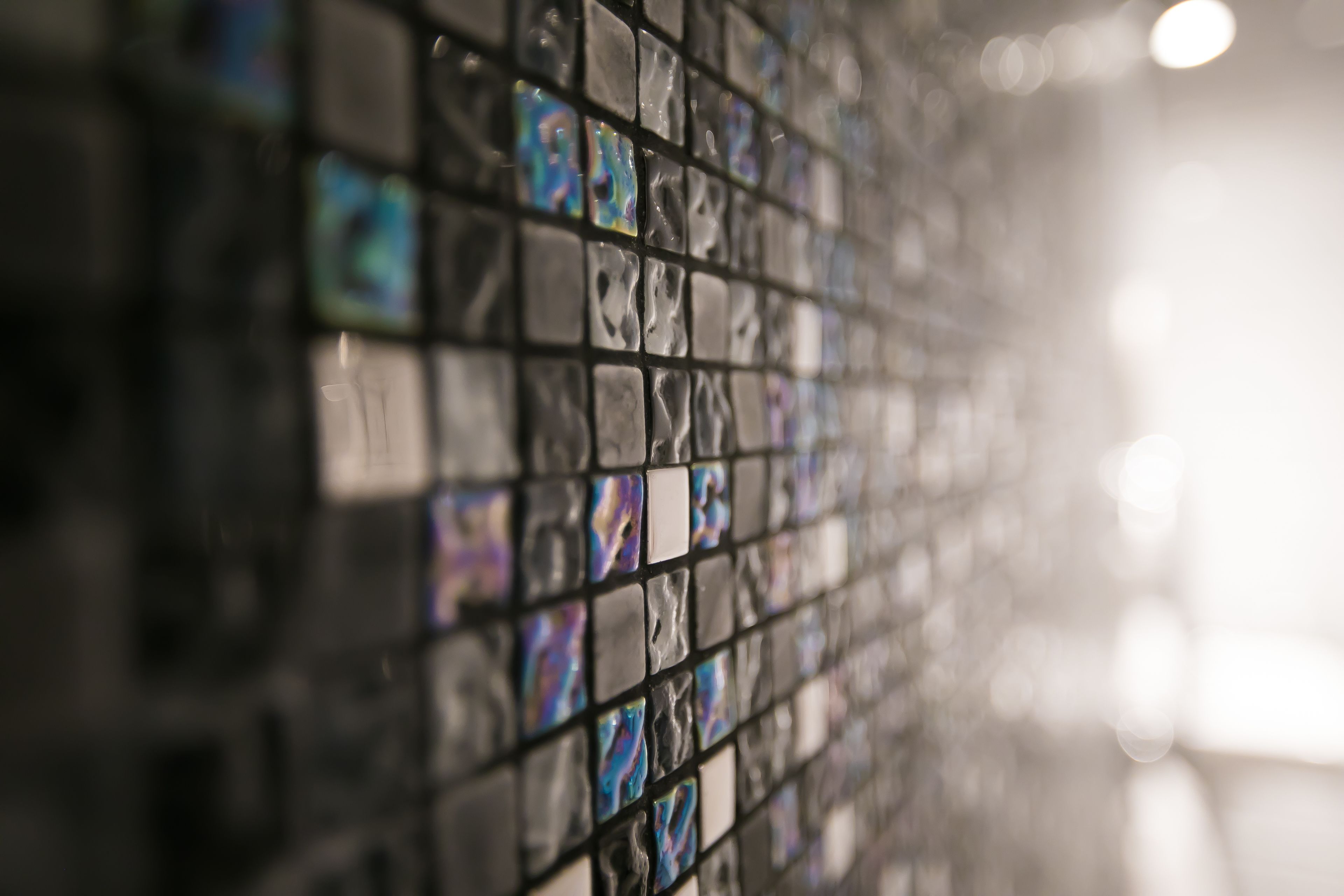 A close-up of a mosaic tile wall with a reflective surface.