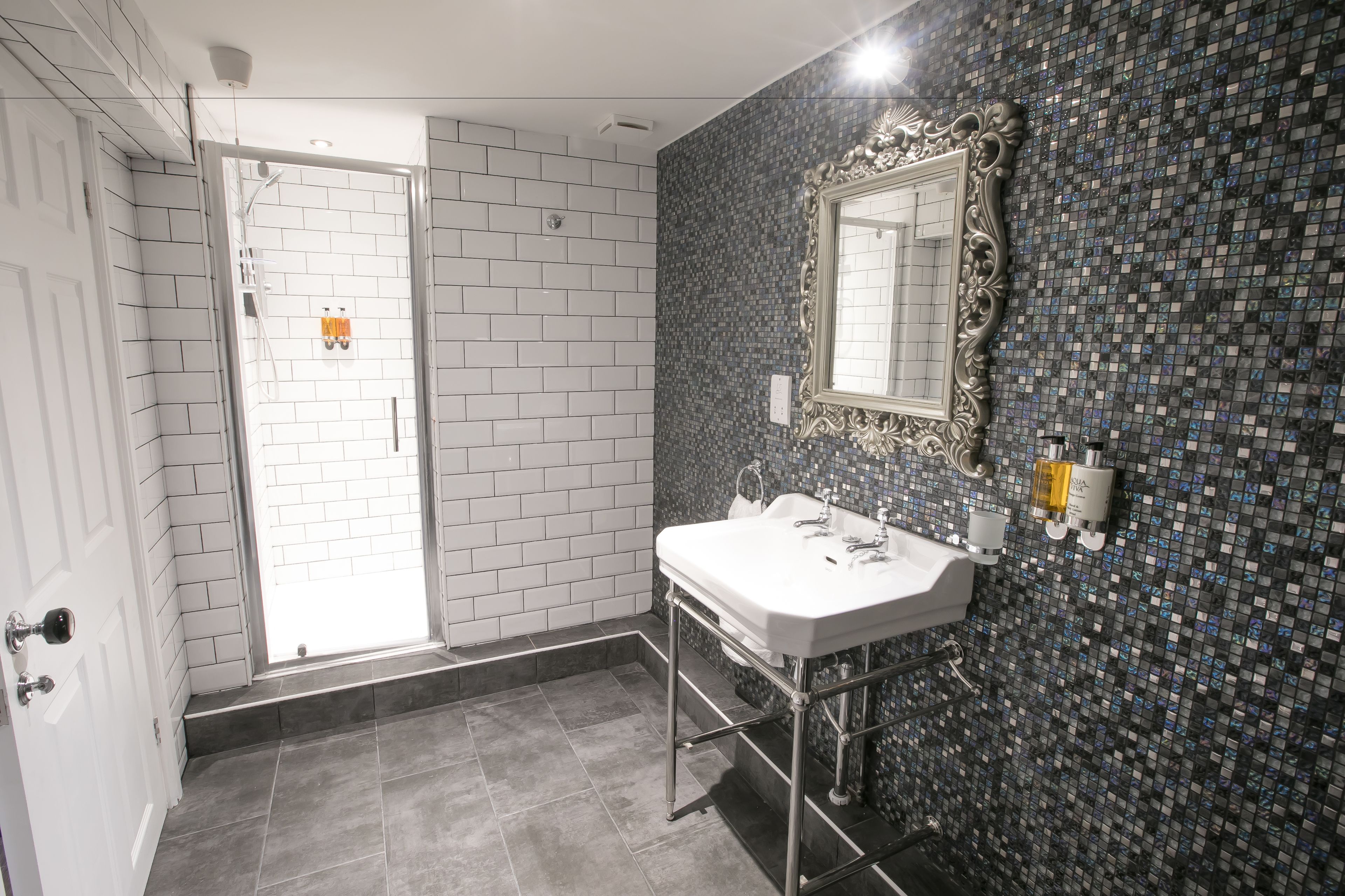 Un baño con lavamanos blanco, un espejo y pared con azulejos.