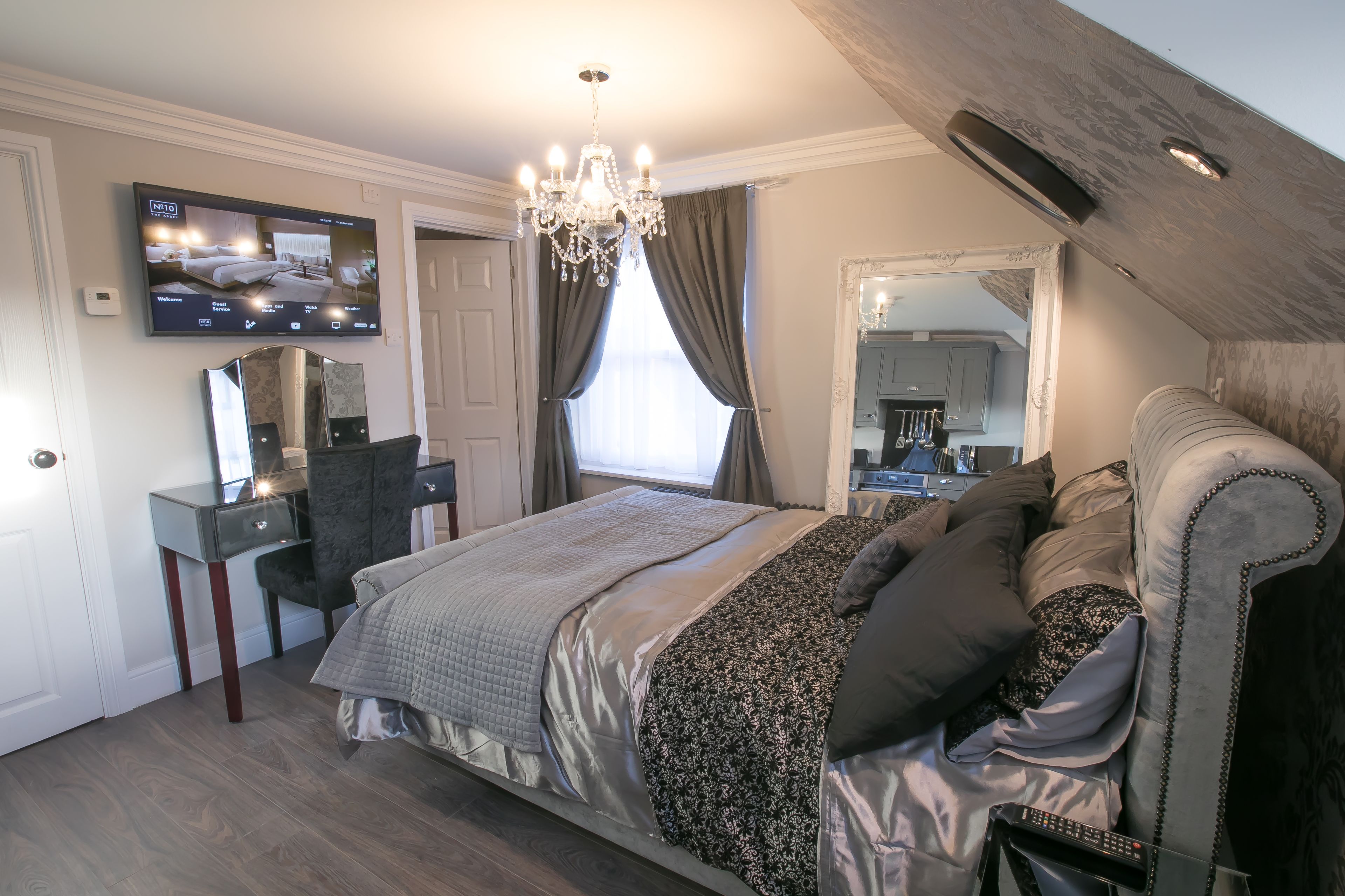 Een slaapkamer met een bed, een aan de muur bevestigde televisie, een dressoir en een spiegel.