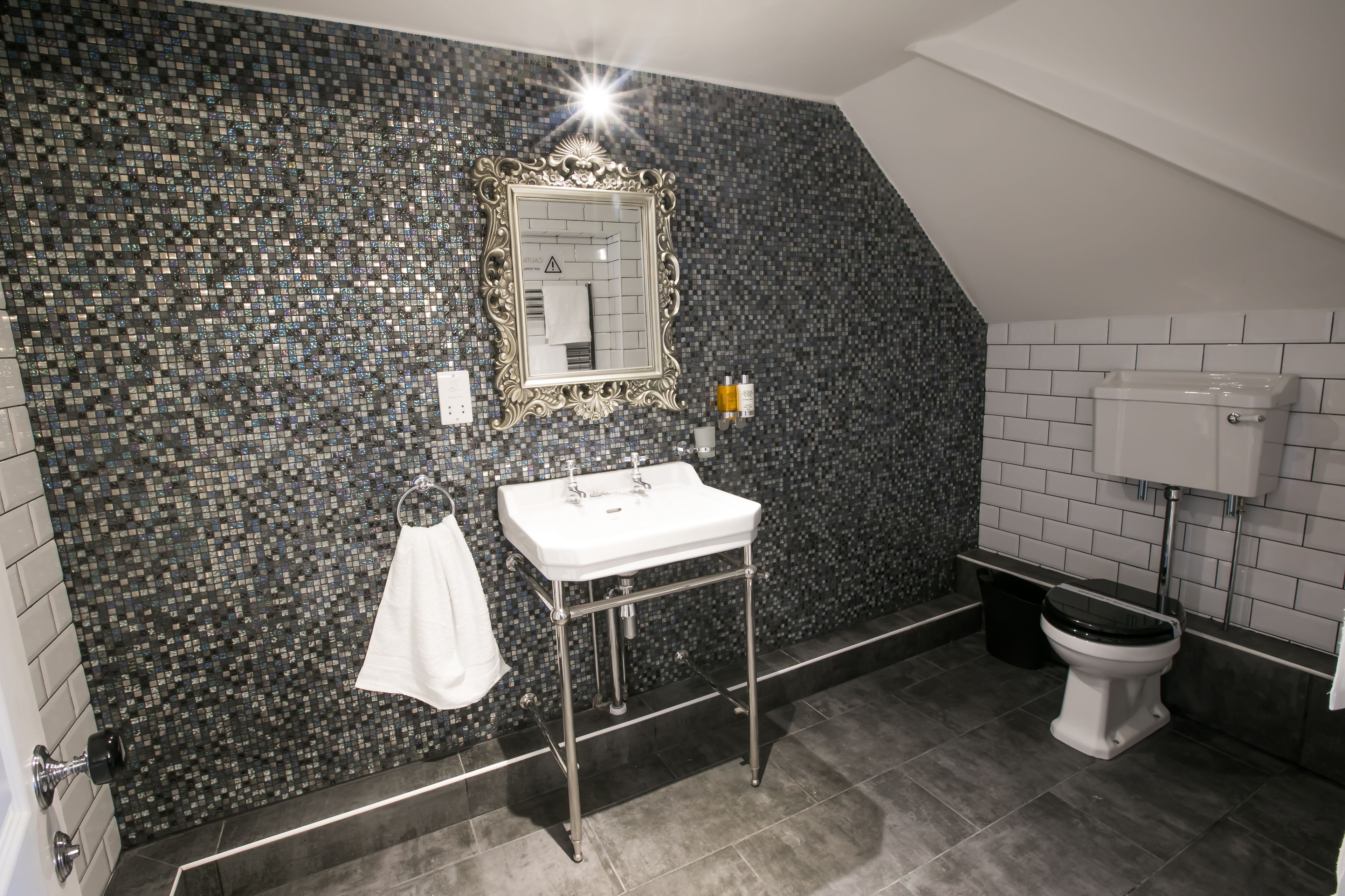A bathroom with a mosaic wall, a white sink, and a toilet.