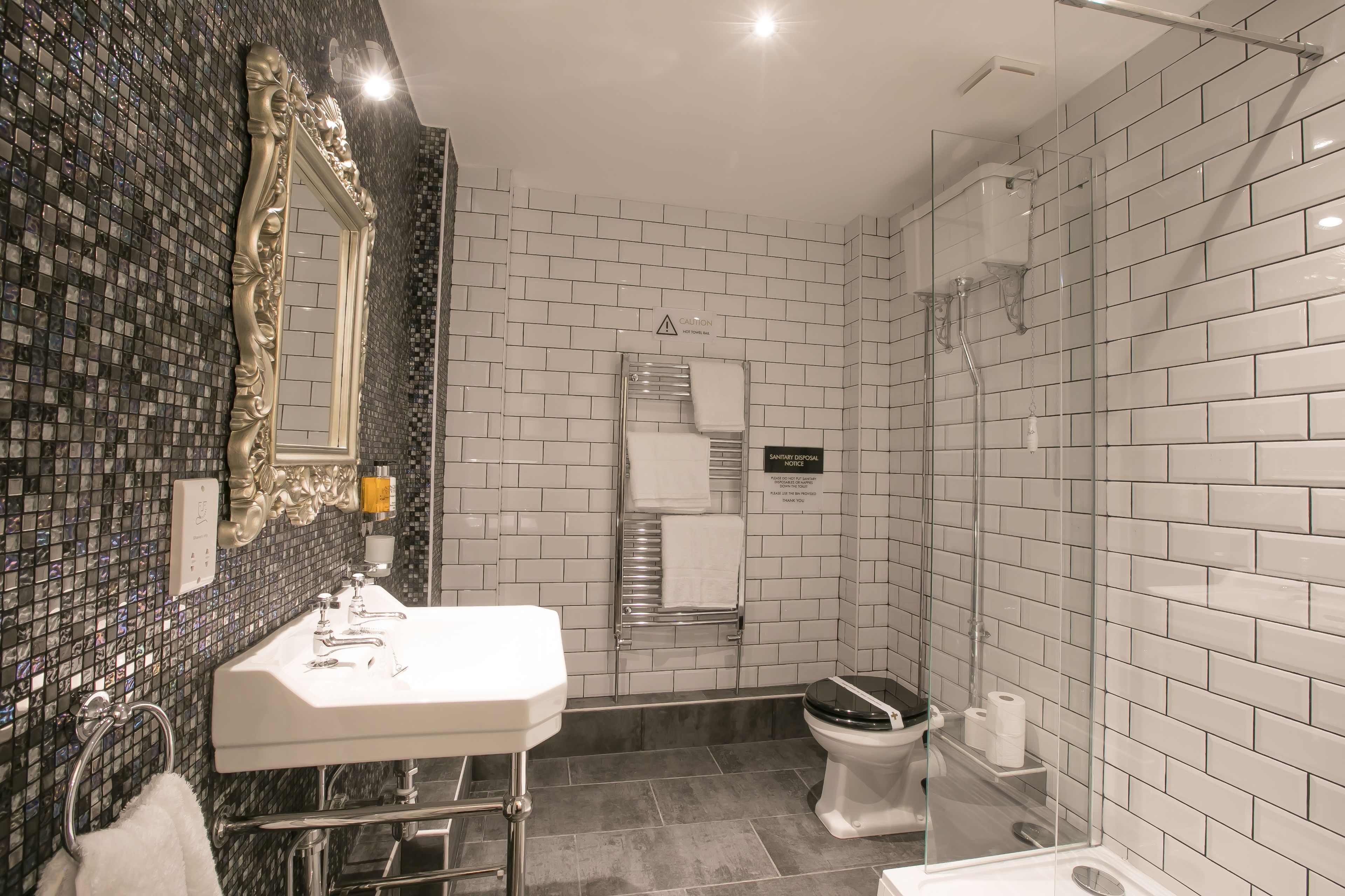 A modern bathroom with a large mirror, a white sink, a toilet, and a glass-enclosed shower area.