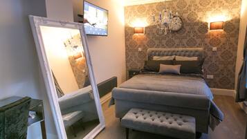 A bedroom with a large bed, a bench, a mirror, a TV, and a chandelier.