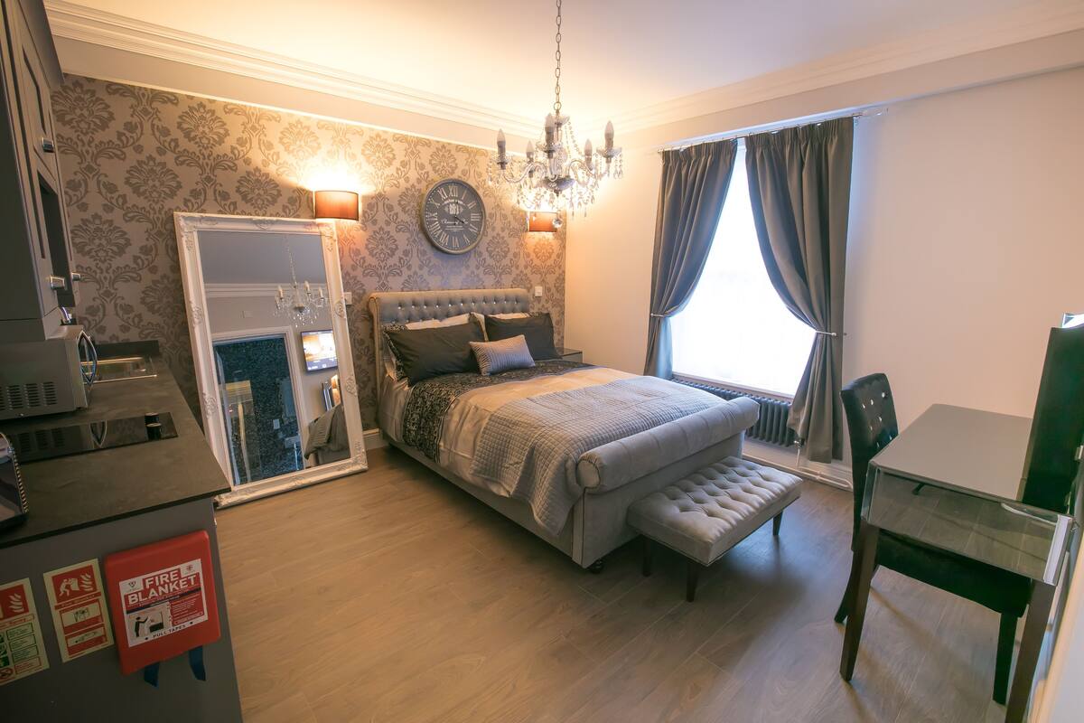 A bedroom with a bed, a mirror, a chandelier, a dining table, and a fire blanket sign.