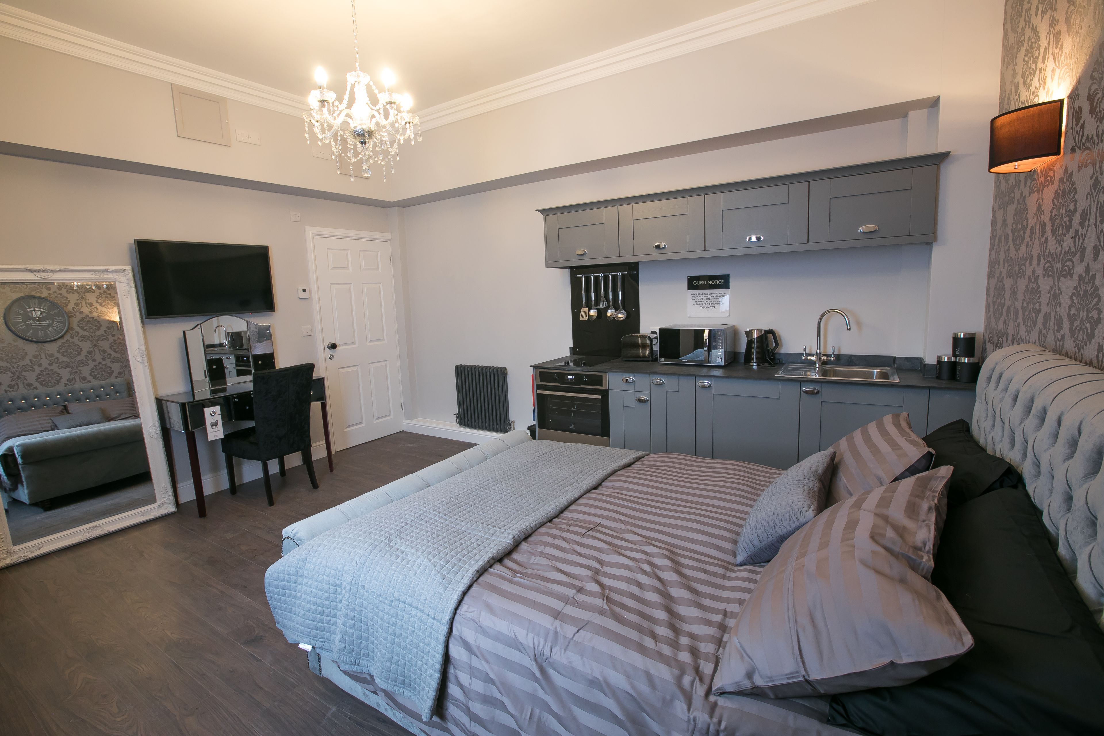 A bedroom with a large bed, a desk, and a kitchenette.