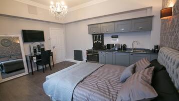 A bedroom with a large bed, a desk, and a kitchenette.