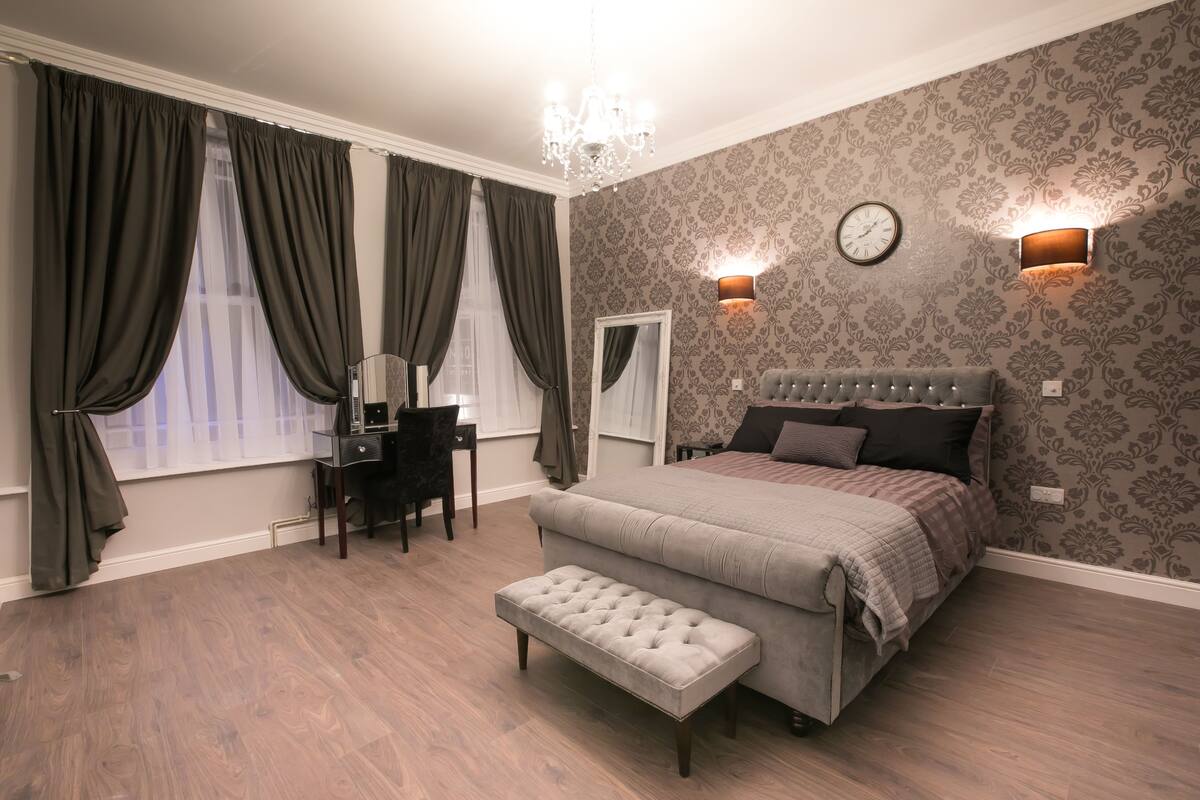 A bedroom with a large bed, a bench, a desk, and two wall-mounted lights.