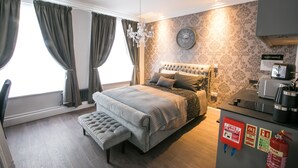 A bedroom with a large bed, a bench, a chandelier, a clock, and a fire safety sign. - Number 10 The Abbey (Wymondham)