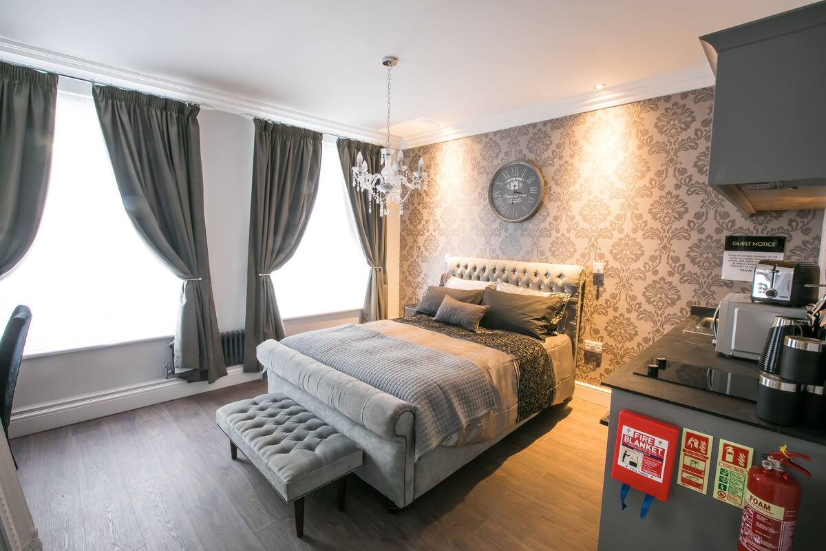 A bedroom with a large bed, a bench, a chandelier, a clock, and a fire safety sign.