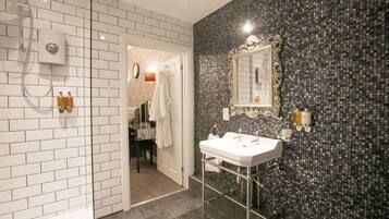 A bathroom with white tiled walls, a black mosaic backsplash, a white sink, and a shower area.