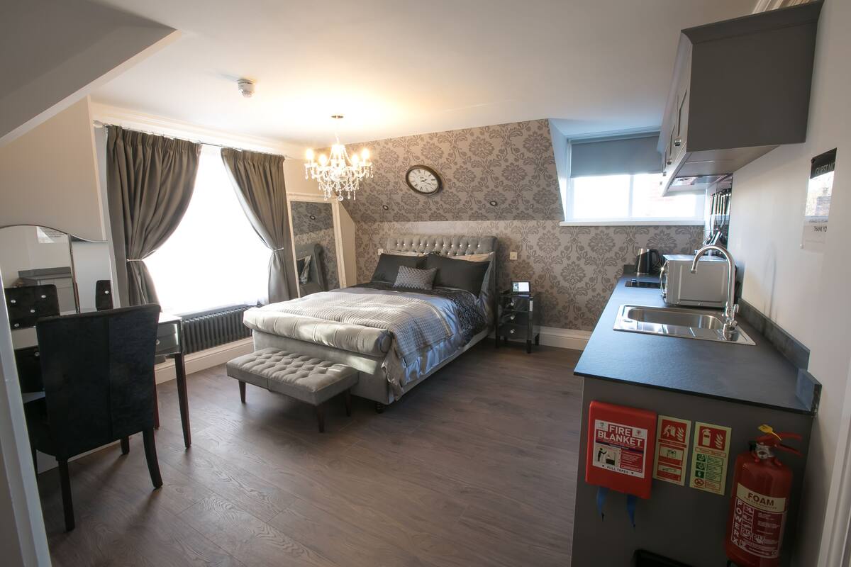 A compact bedroom with a bed, a desk, and a kitchenette.