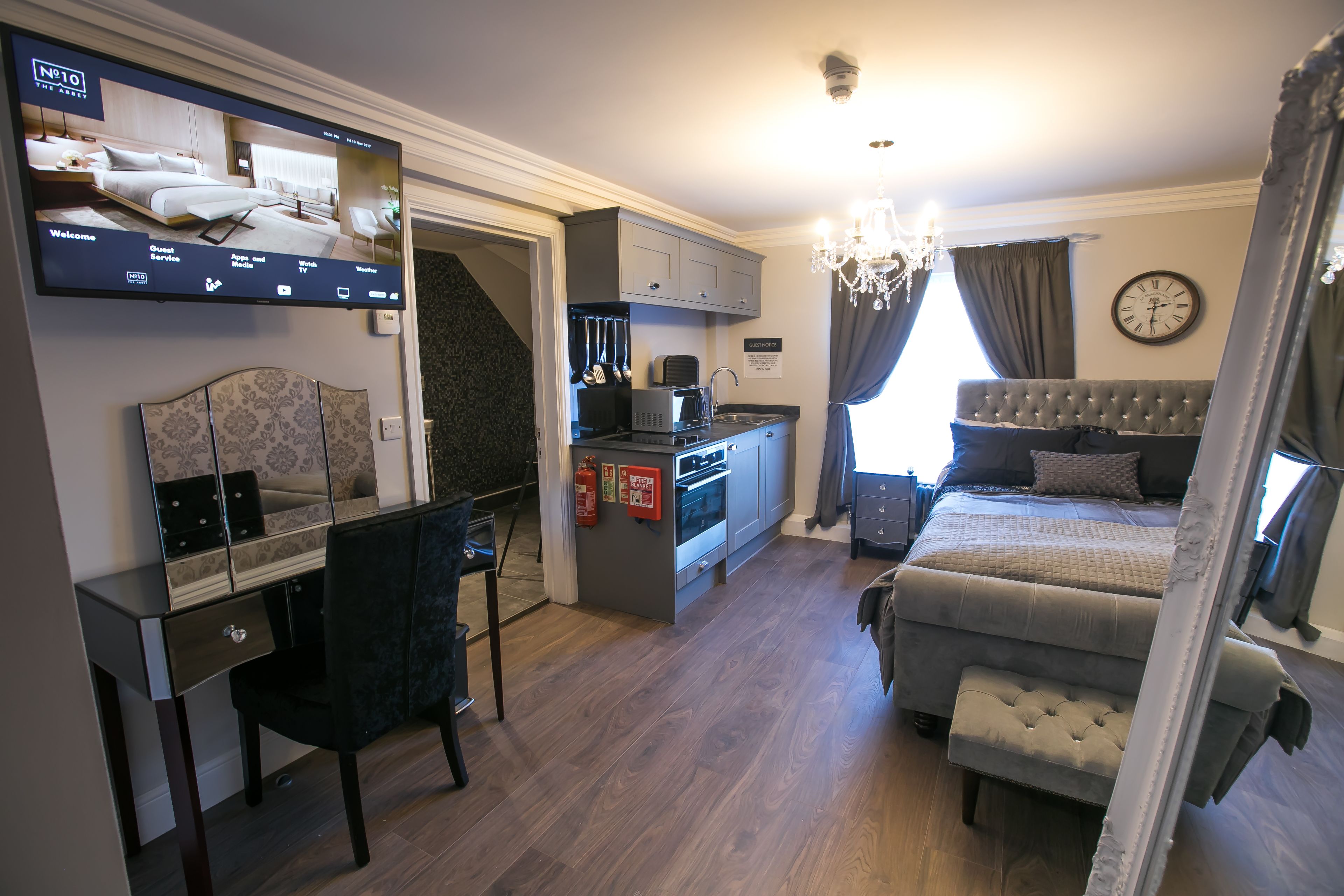 A hotel room with a bed, a desk, a television, a kitchenette, and a bathroom.