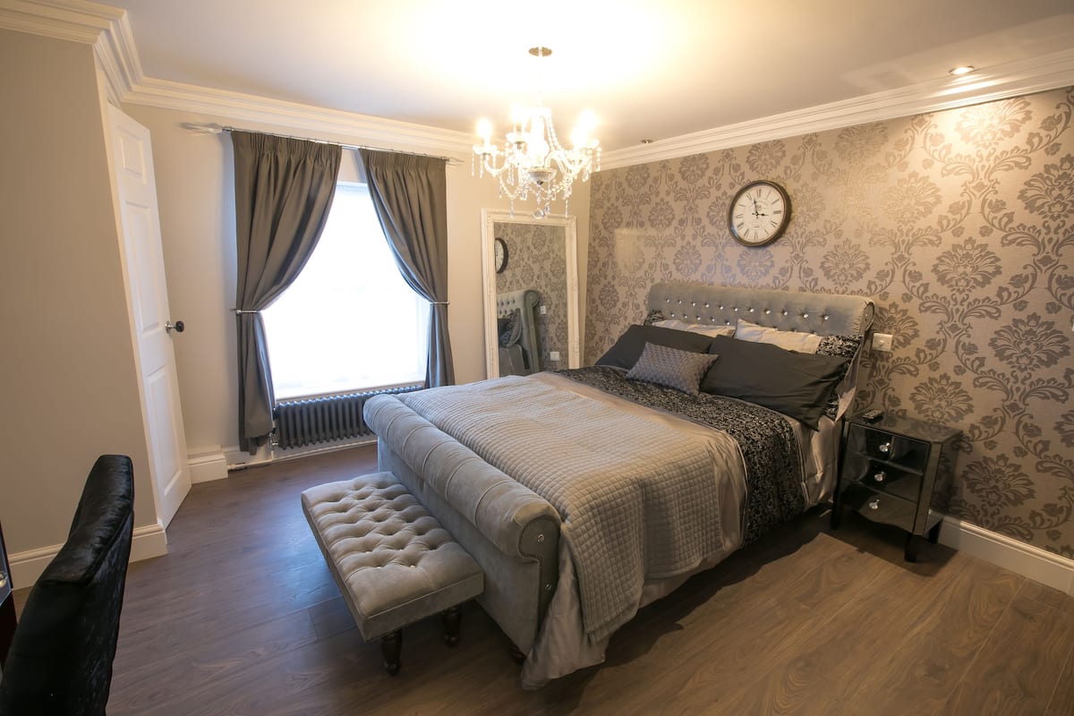 A bedroom with a large bed, a bench, a nightstand, and a mirror.