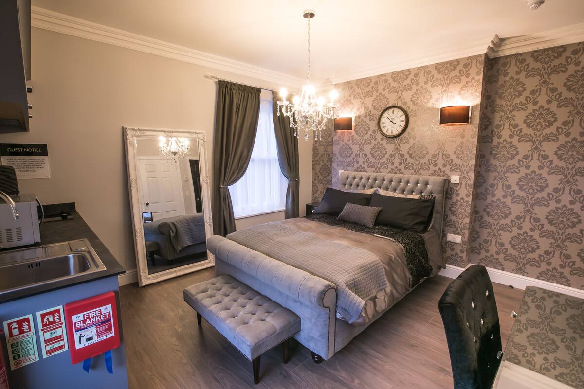 A bedroom with a bed, bench, chandelier, and a clock on the wall.