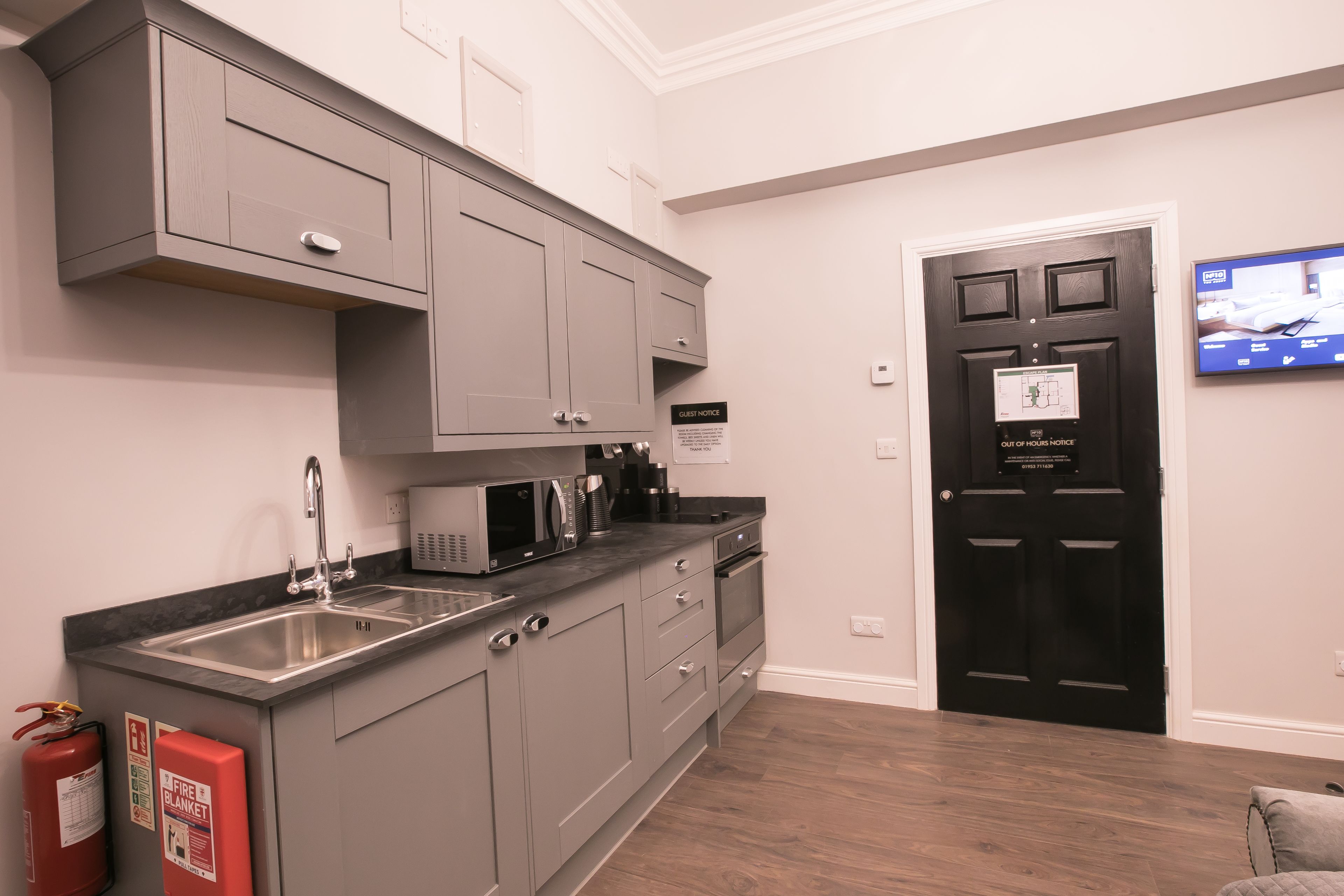 A modern kitchen with grey cabinets, a stainless steel sink, and a black door with a guest notice.