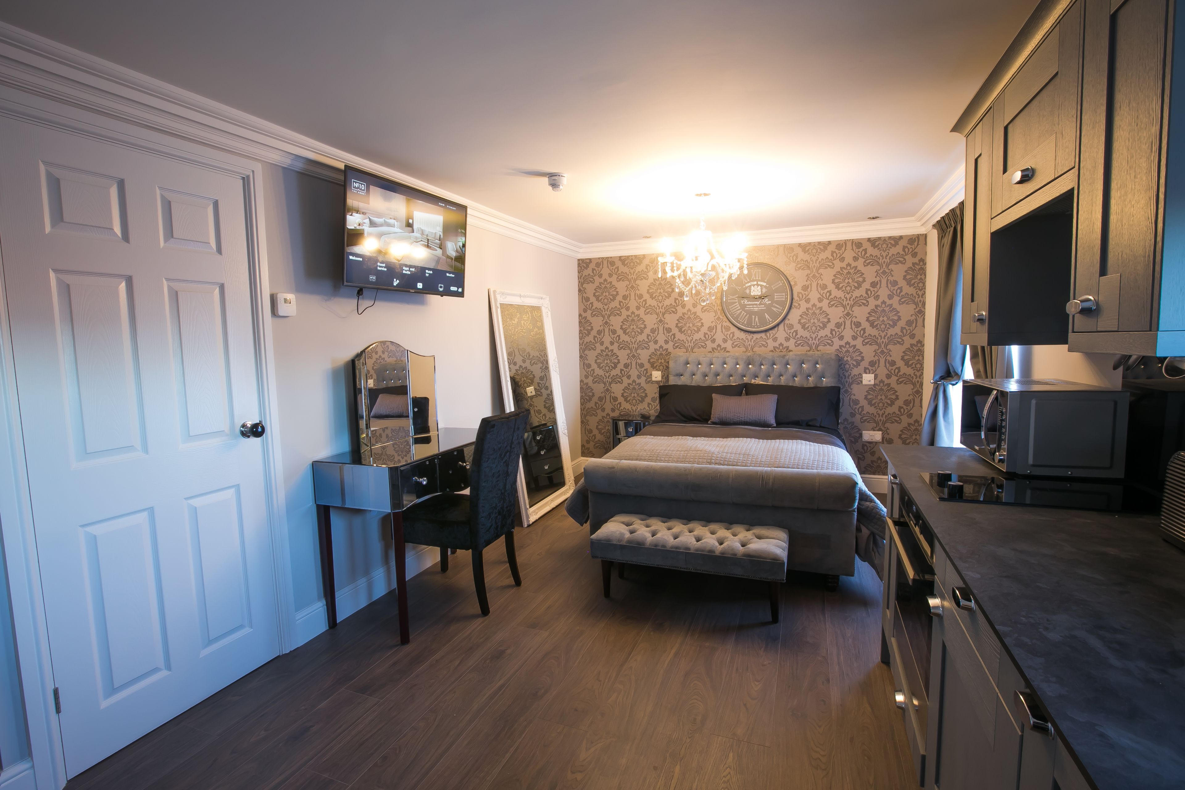 A bedroom with a bed, a desk, a chair, a TV, and a chandelier.